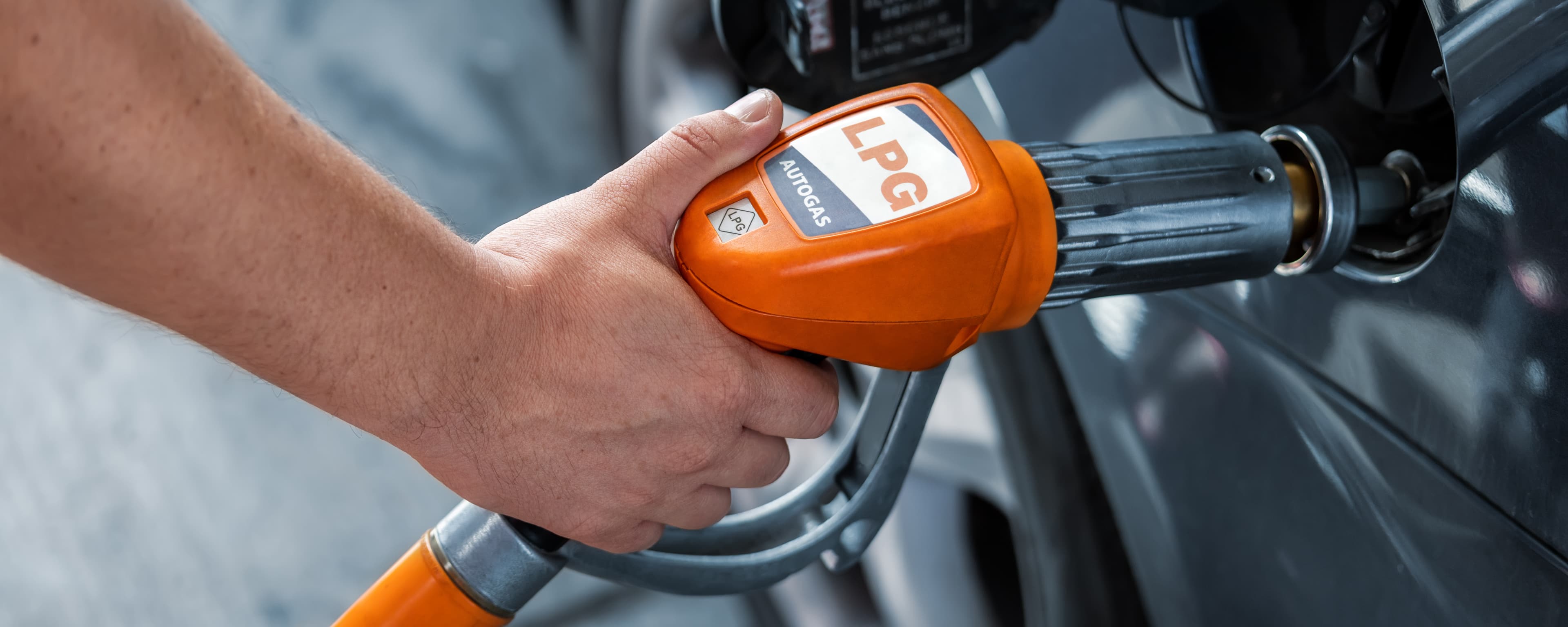 A person is holding an LPG bowser nozzle, filling their car