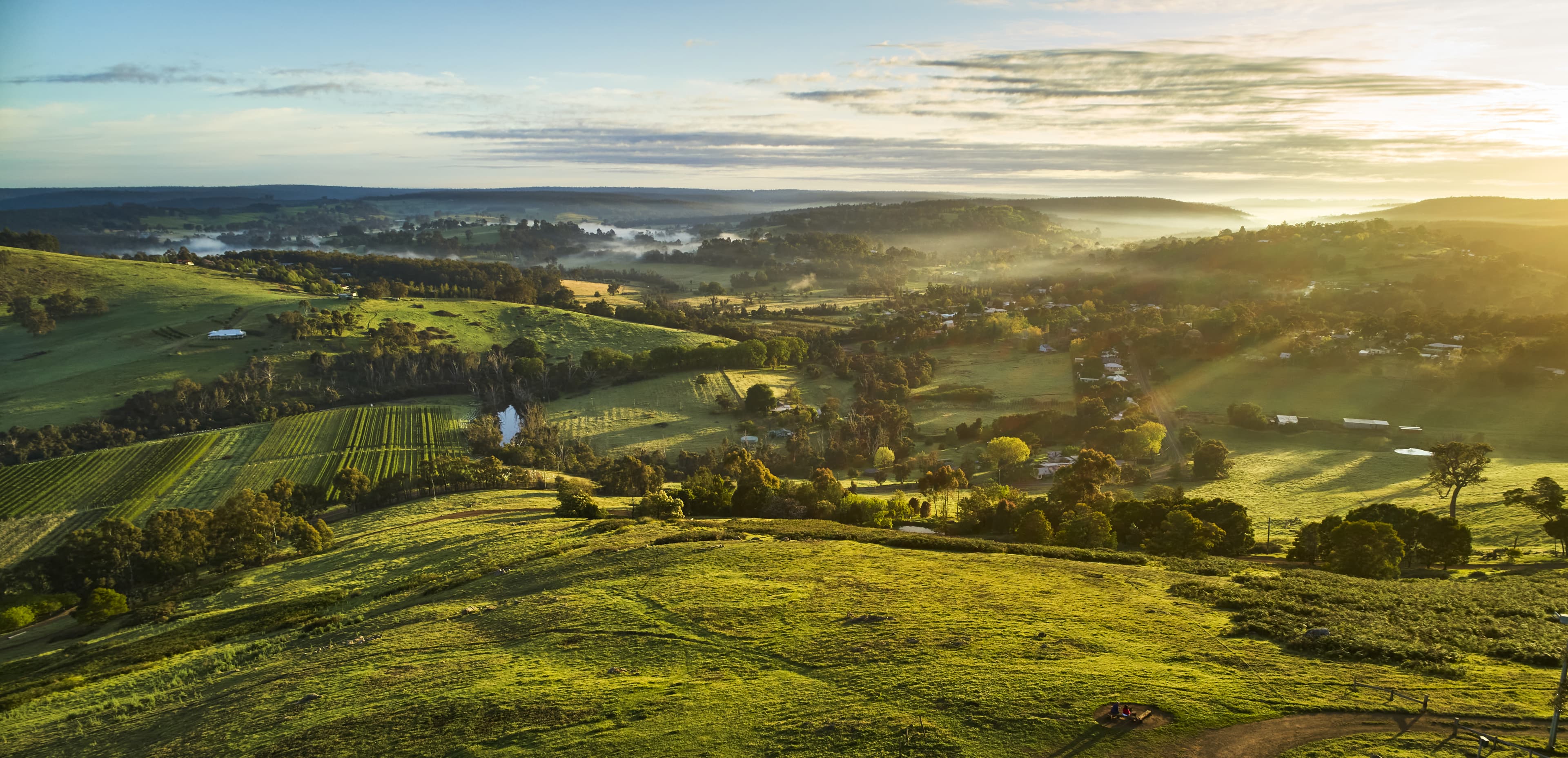 Aerial view of sunrise over Balingup, town in Western Australia, with rolling green hills and mist over a valley.