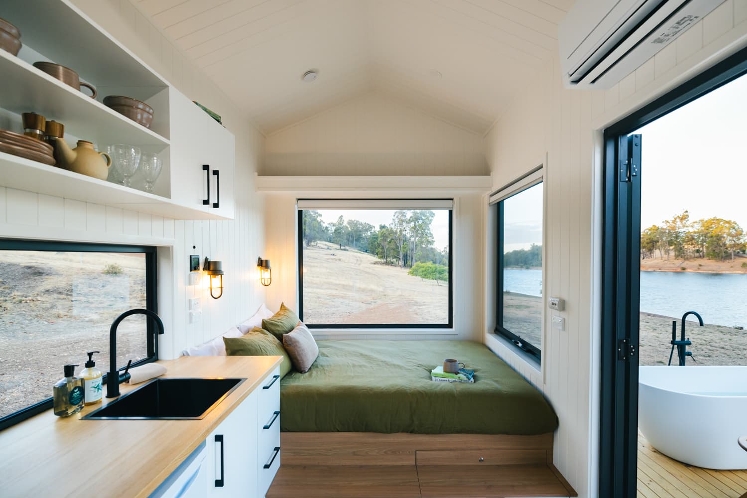 The interior of Tiny Matilda cabin in Bridgetown, showing the bedroom, outdoor view, kitchen and outdoor bath.