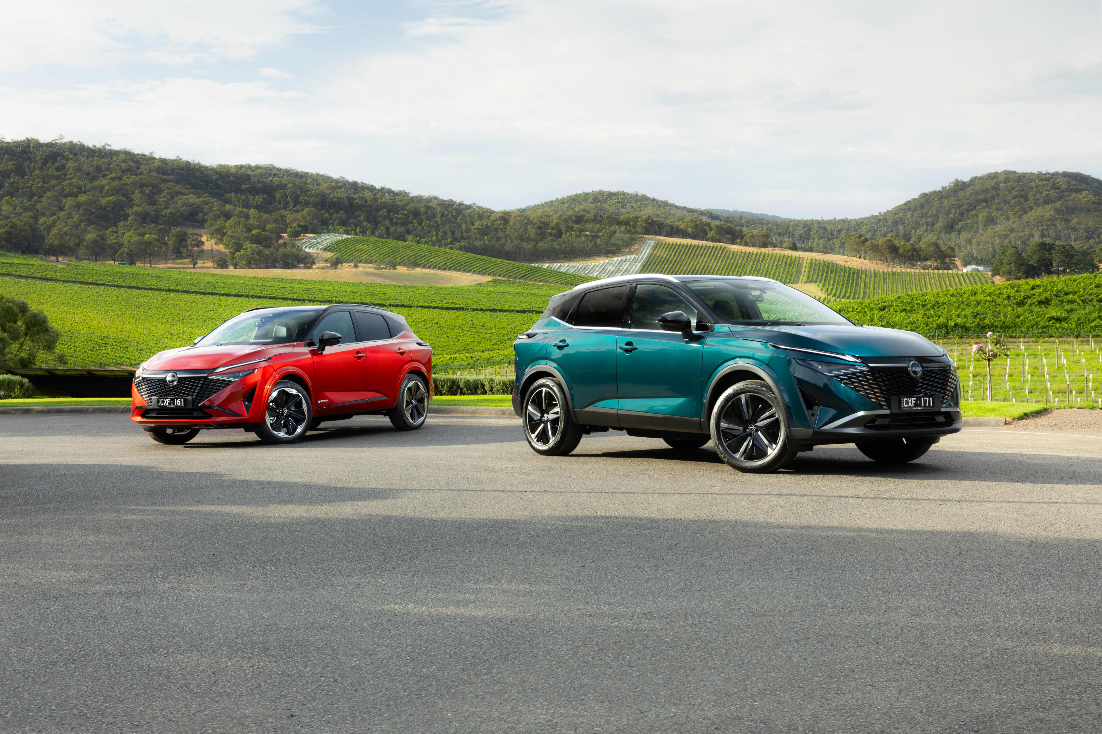 A red and a green Nissan Qashqai SUV parked next to one another in a field.