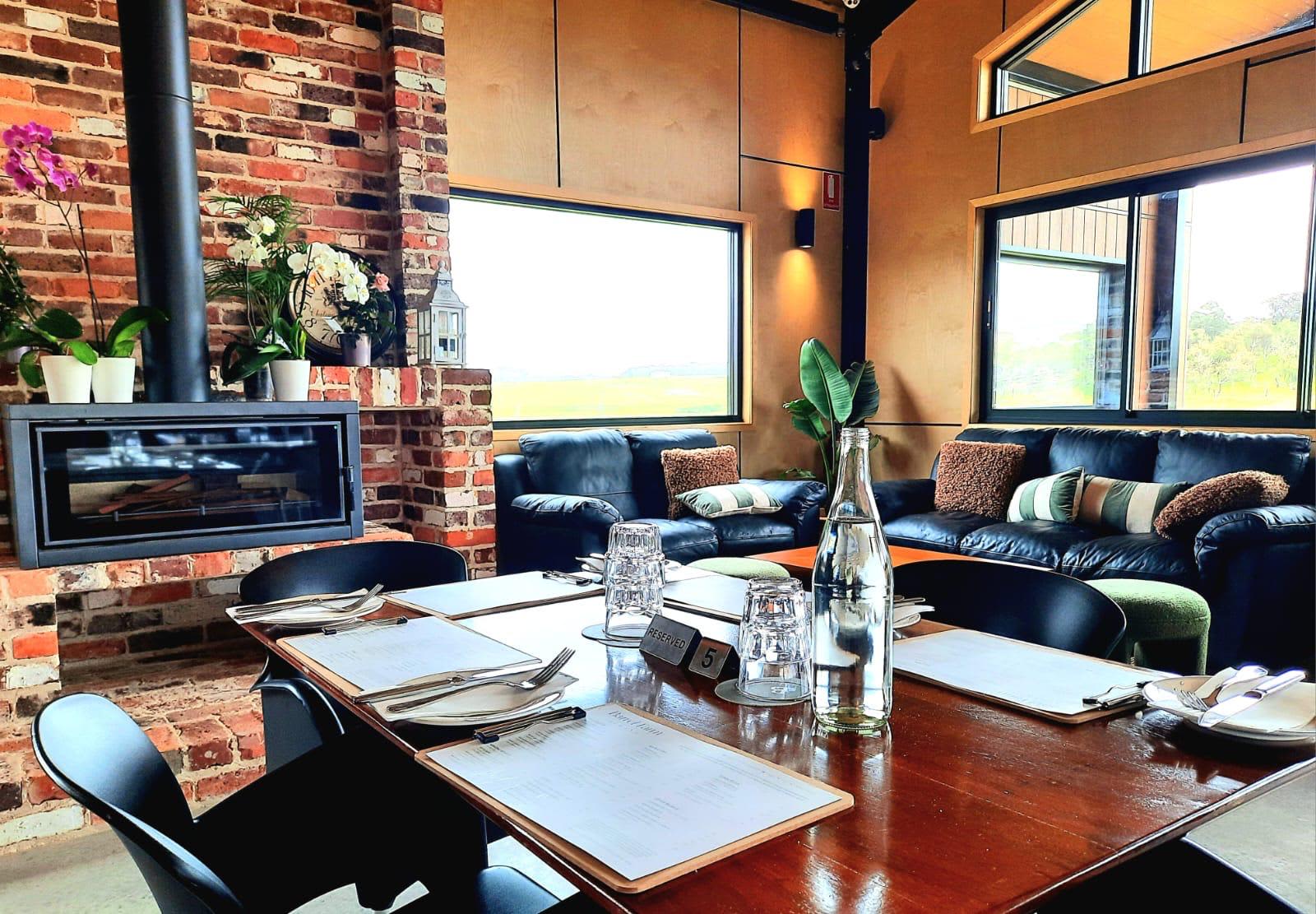 A cosy brick fireplace, lounge and tables set for dinner.