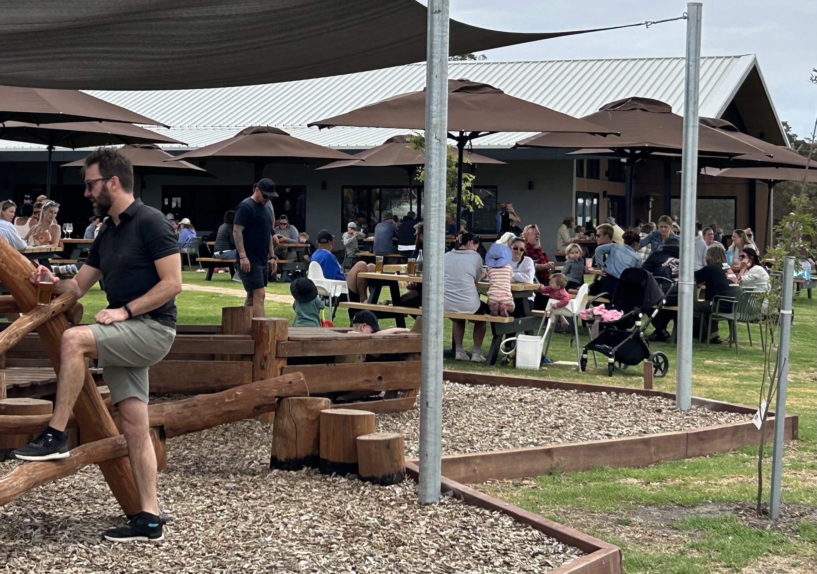 People mingling with friends and family under umbrellas in the outdoor area of The Barrel Farm.