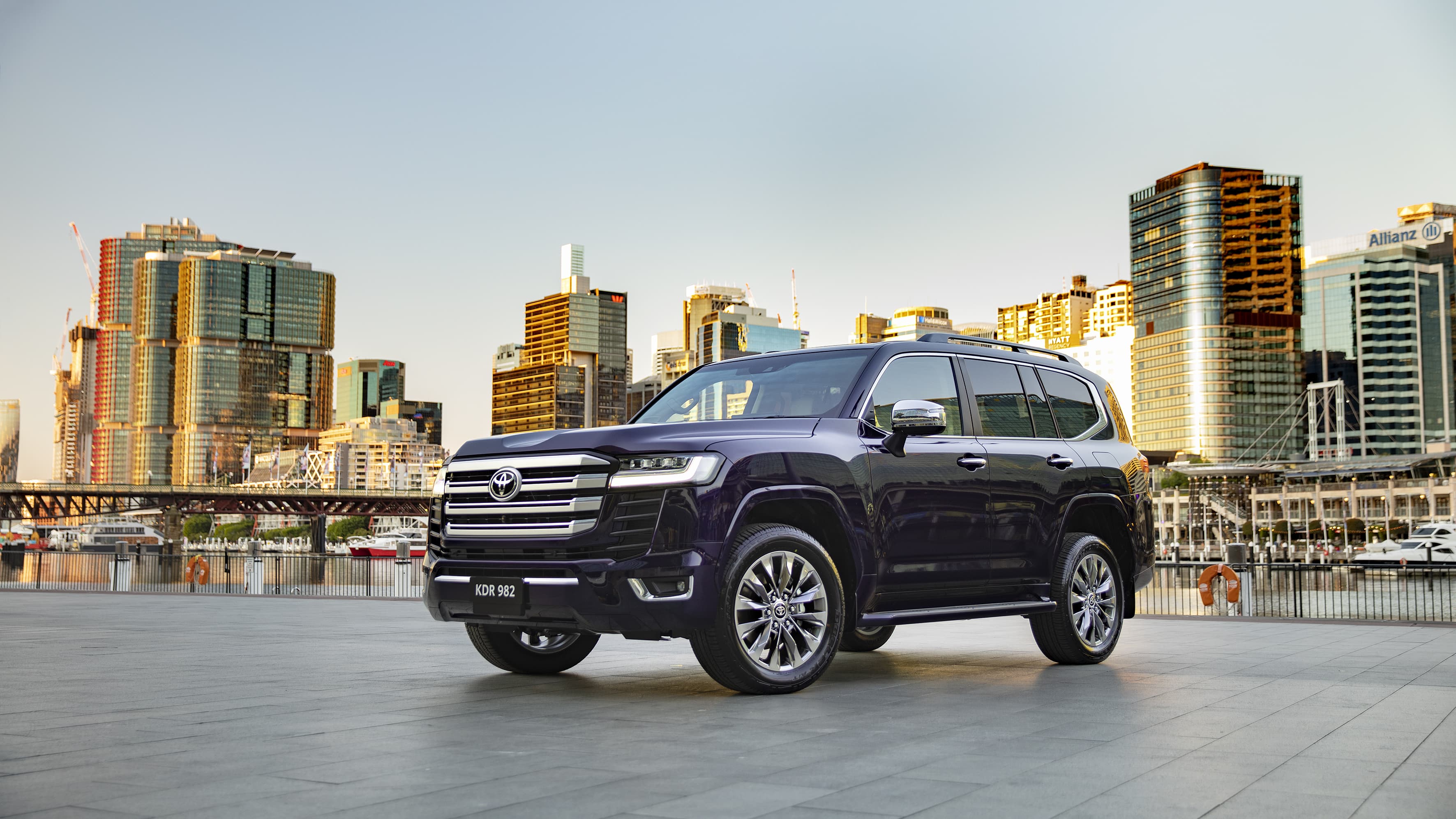 A dark blue Toyota LandCruiser 300 in front of a cityscape