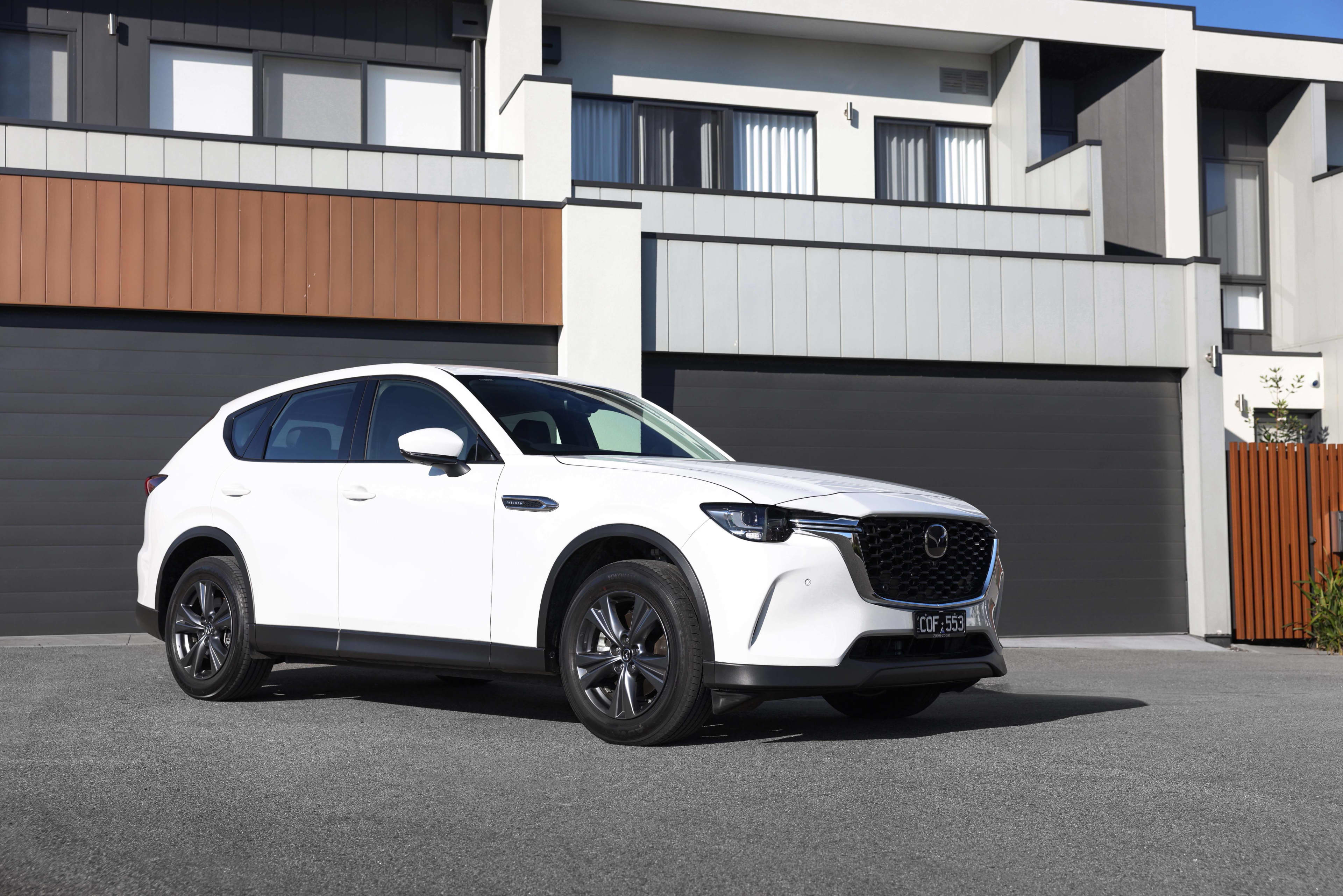 A white Mazda CX60 parked in front of a modern home