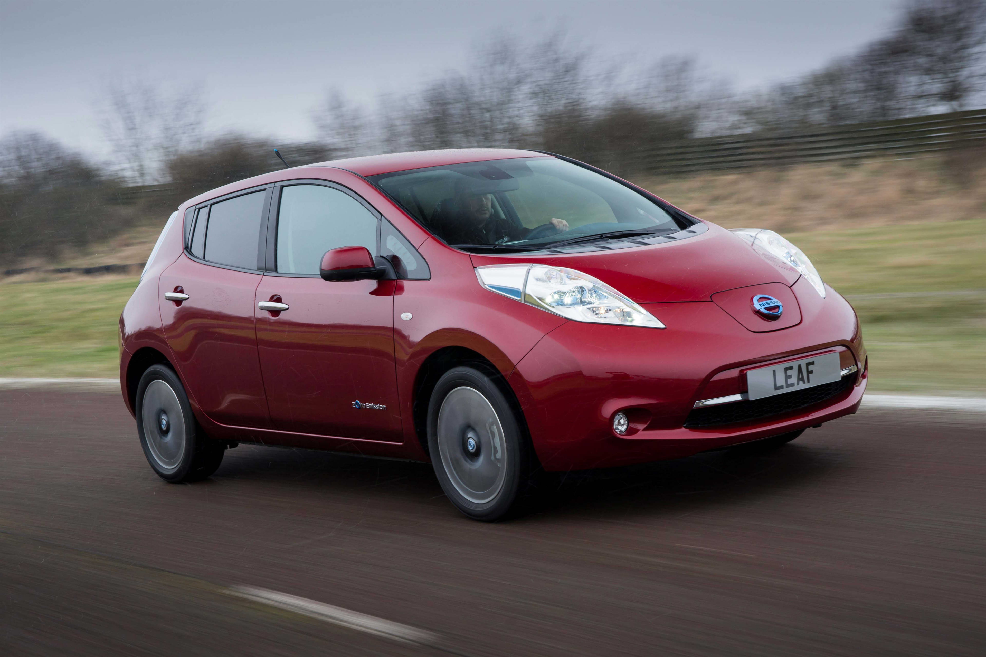 A red Nissan Leaf driving on a country road