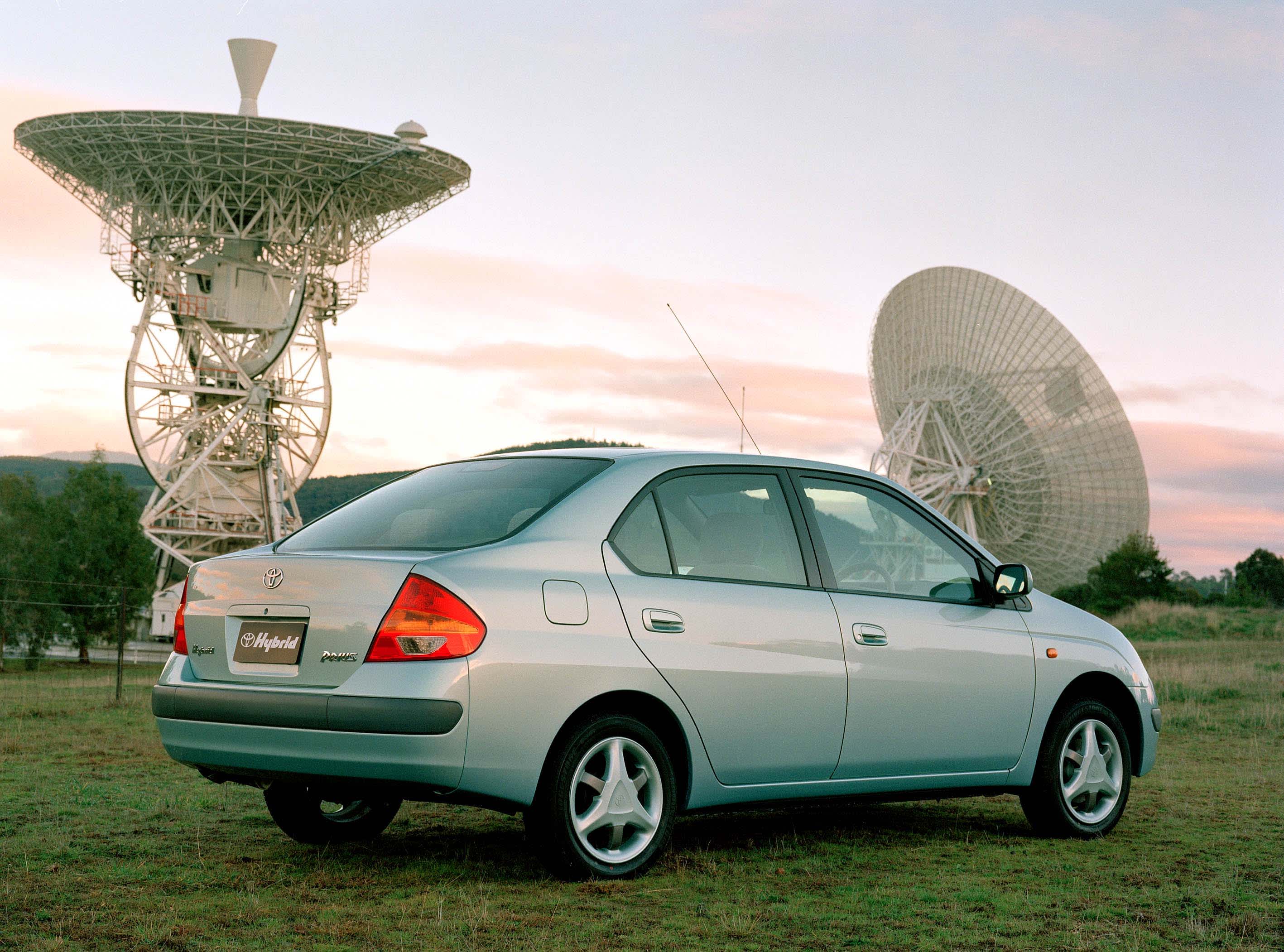 An older model Toyota Prius in front of satellite dishes
