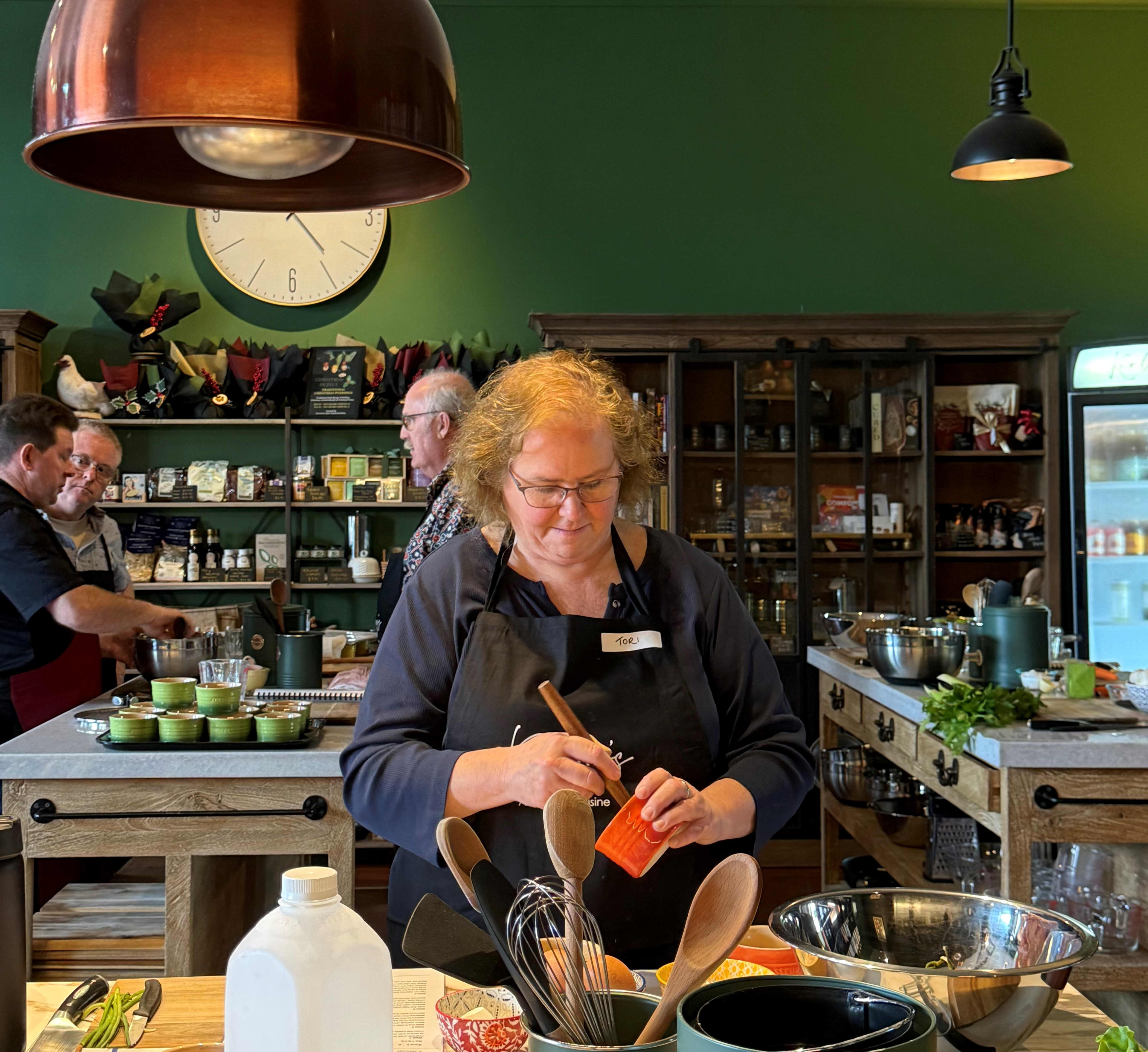 A woman cooking in cooking kitchen with other guests learning how to cook at kitchen bench from executive chef