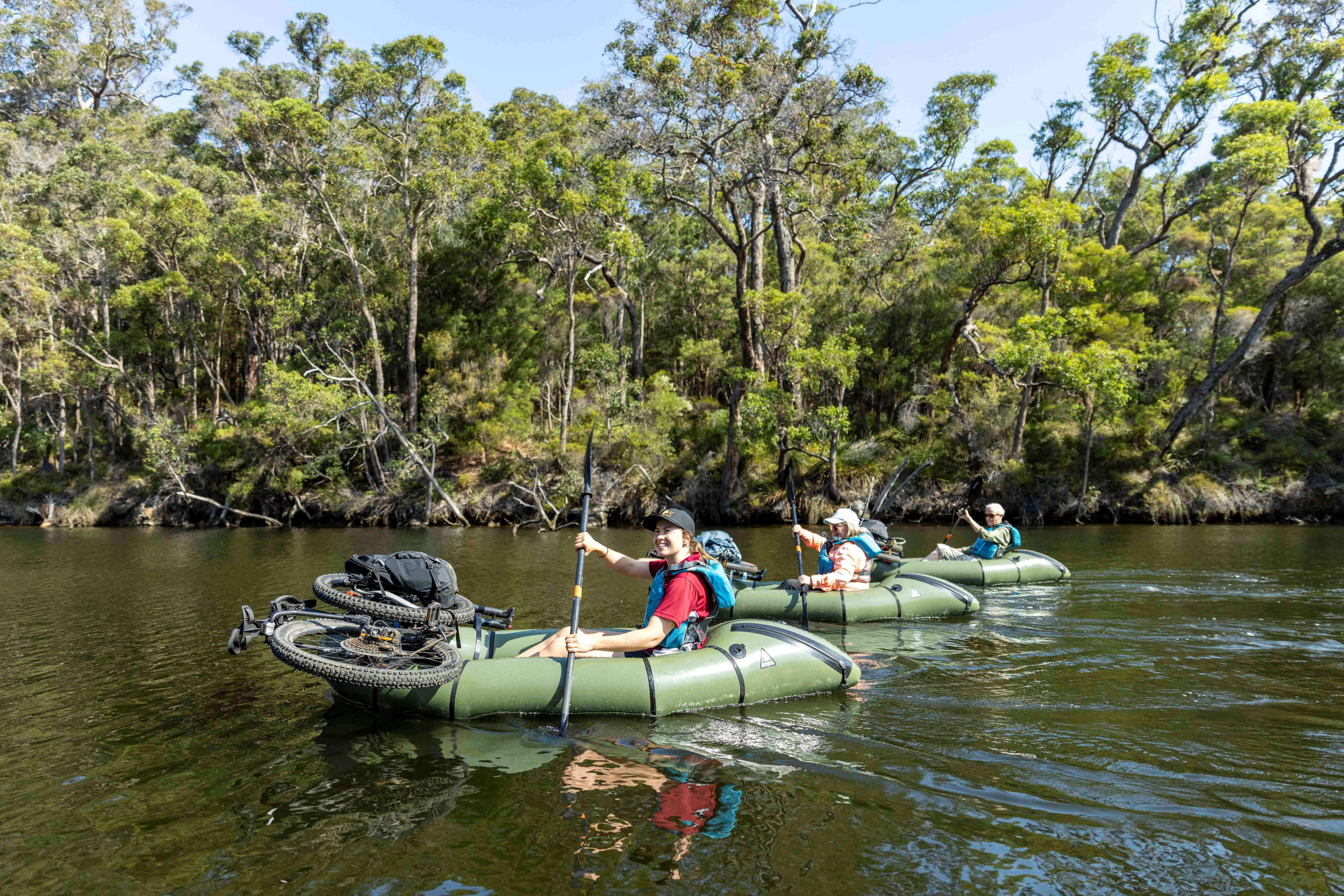 People paddling inflatable kayaks with bikes strapped to the kayak.