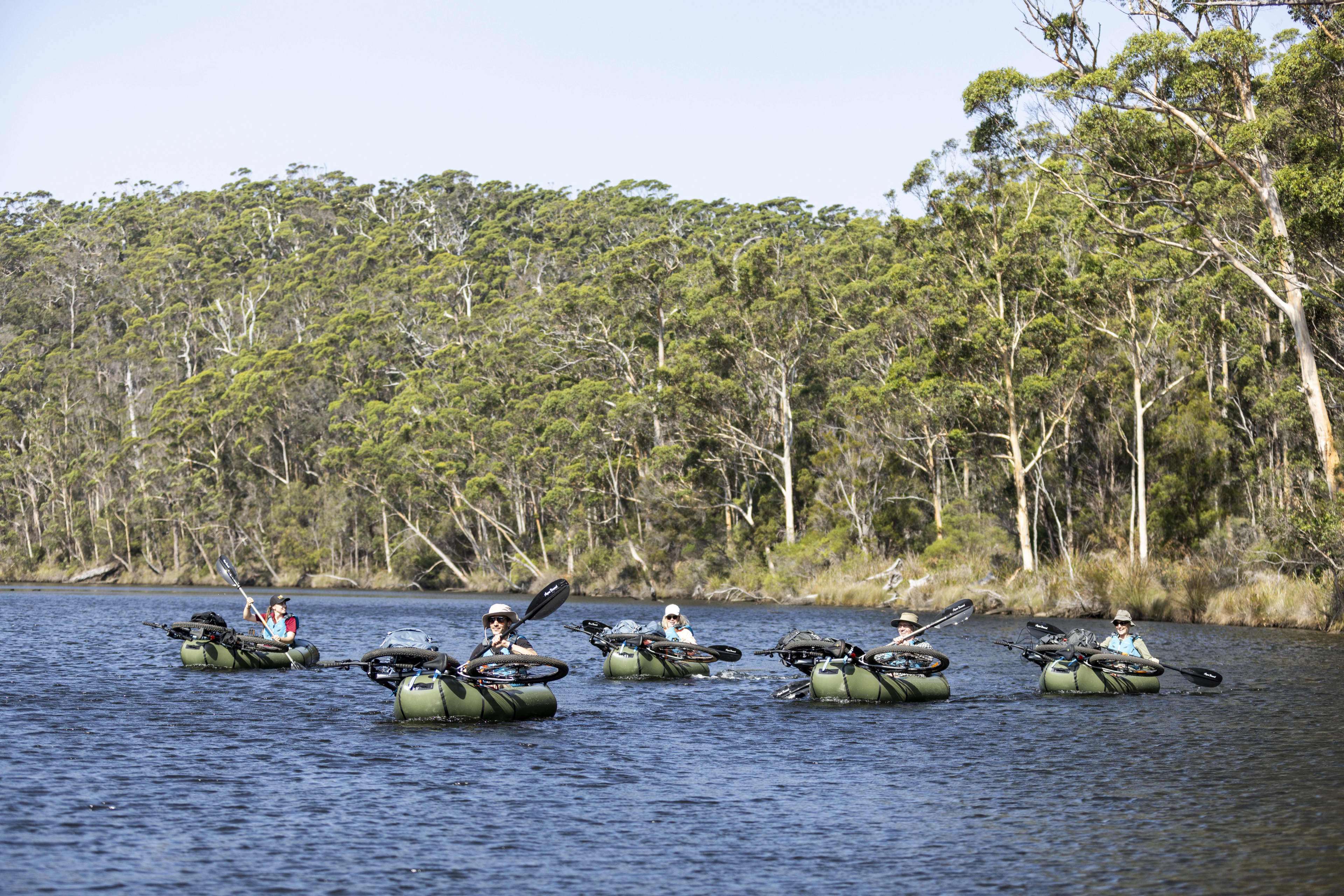 People paddling inflatable kayaks with bikes strapped to the kayak