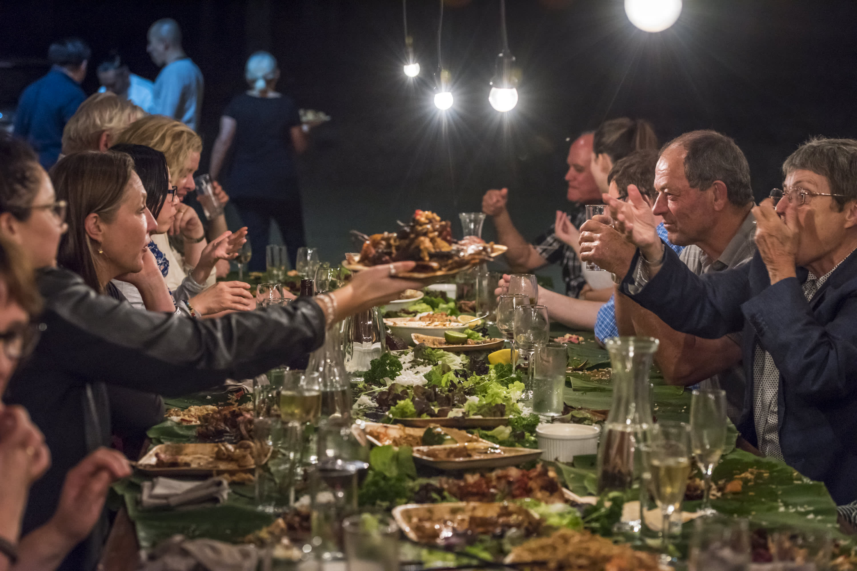 A group of people sitting at an outdoor dining table with many  food dishes on the table
