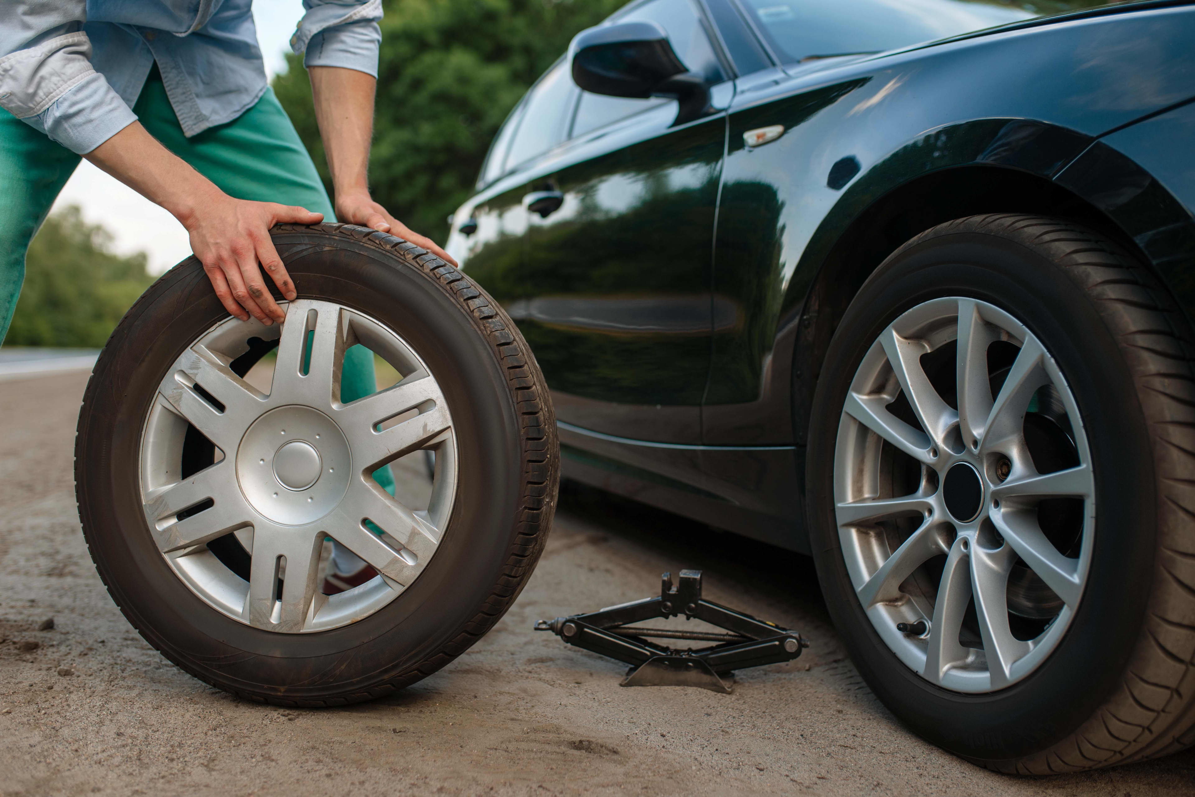 A person is changing a flat tyre with a full-size spare tyre