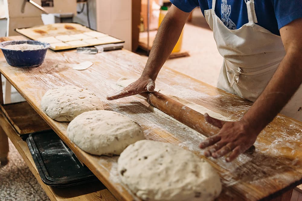 A baker kneading dough on a wooden benchtop