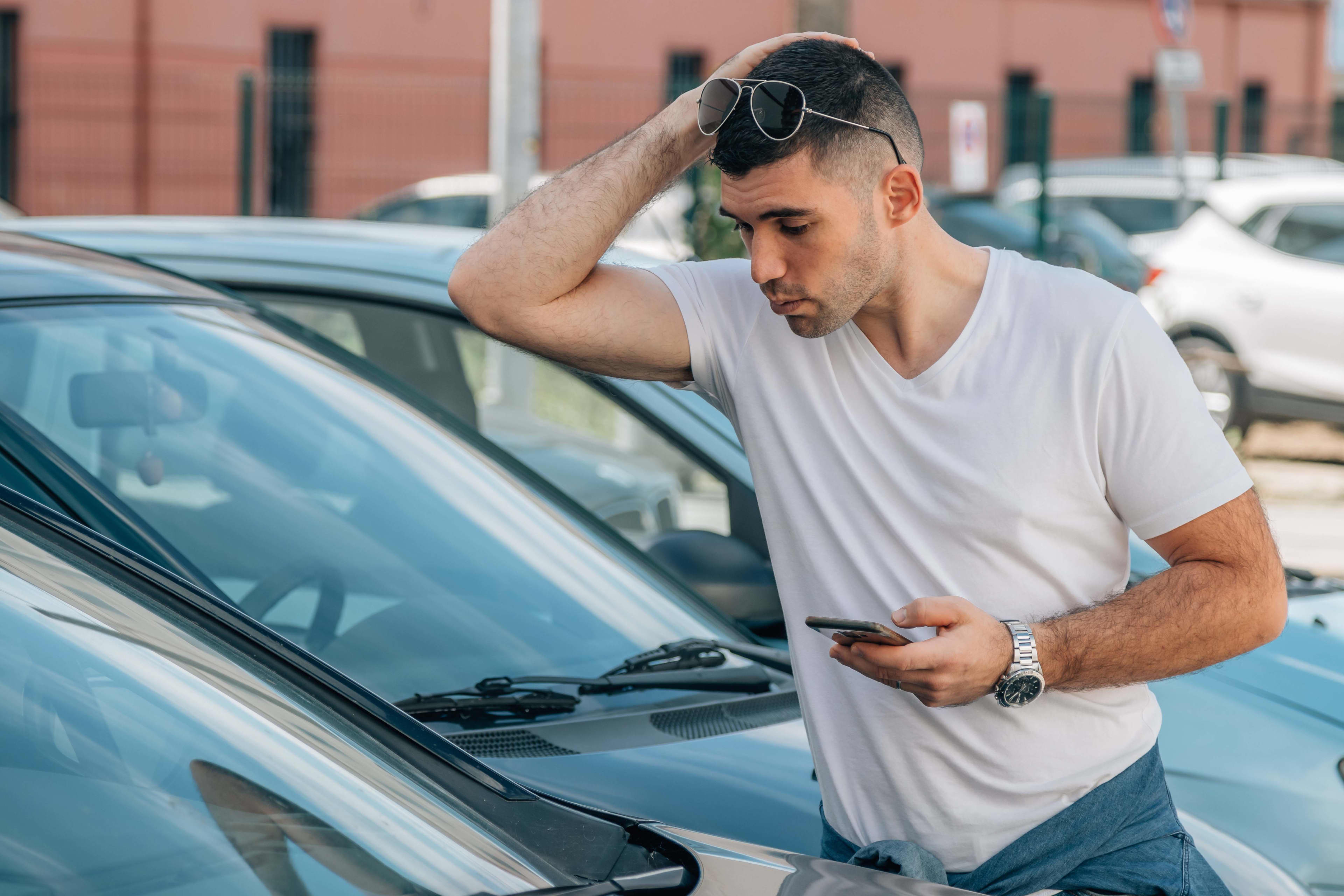 A young man is looking inside a car window in a yard.