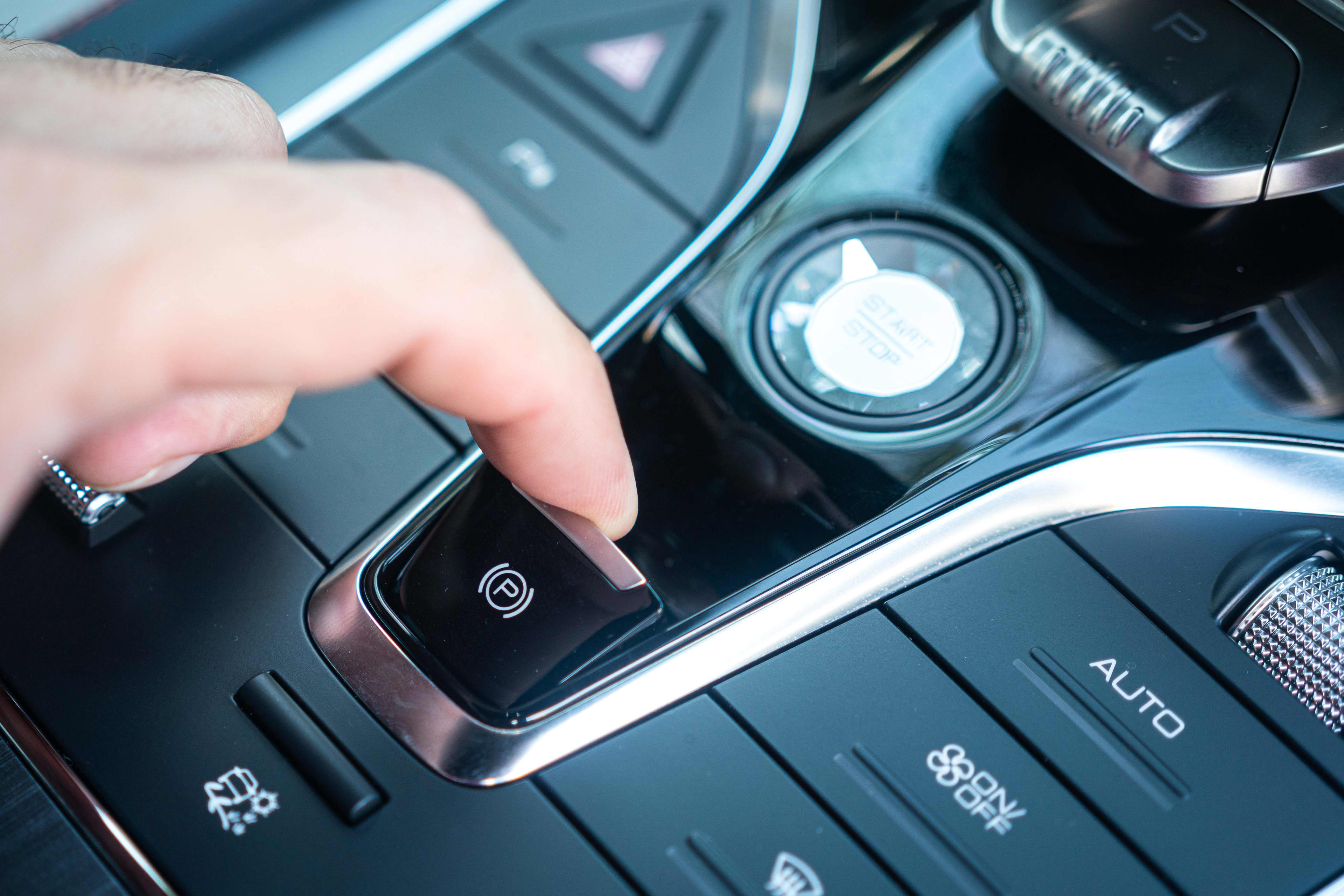 A close up of a driver's hand pulling the electronic parking brake button in a car.