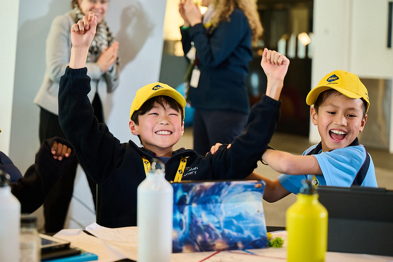 Two 2025 Hackathon students cheering at desk.
