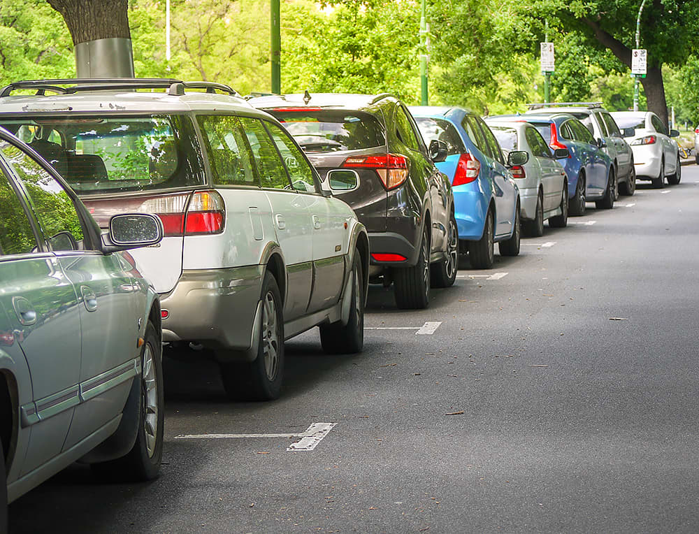 A leafy city street with cars parked on the roadside.