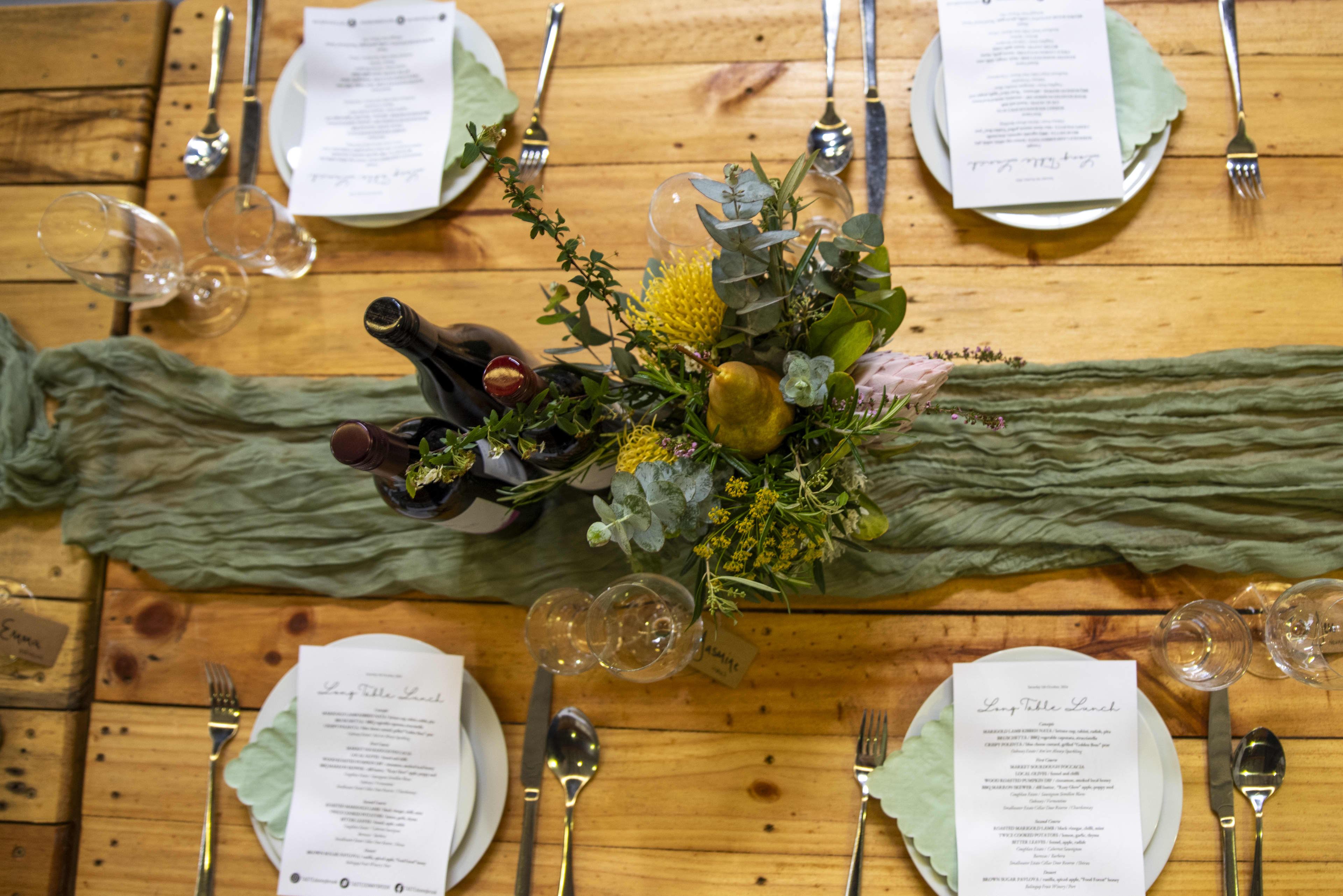 Crockery, cutlery and glassware on table with bottles of wine and floral table settings.