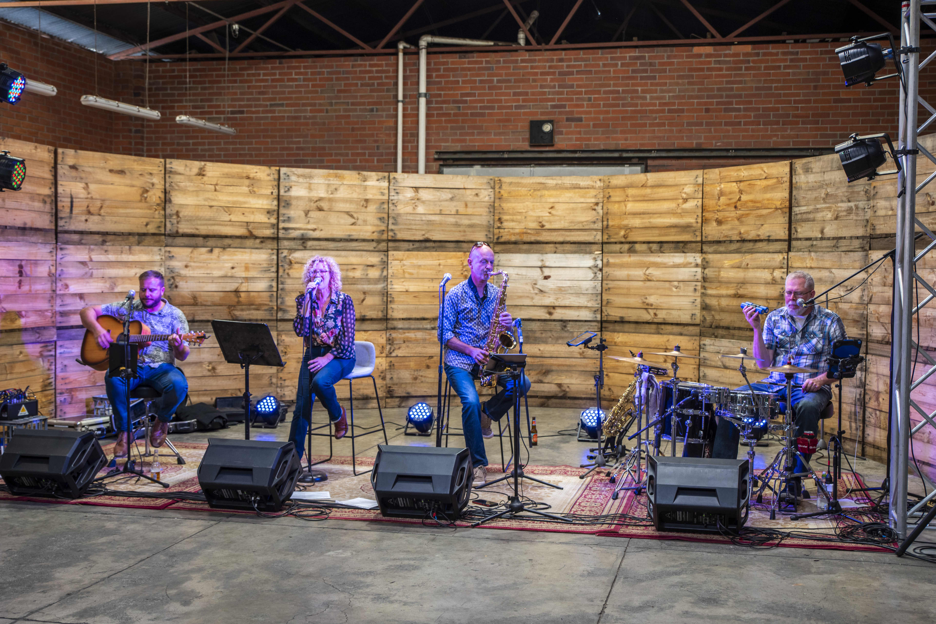 A group of four band members with saxophone, guitar and instruments performing at event