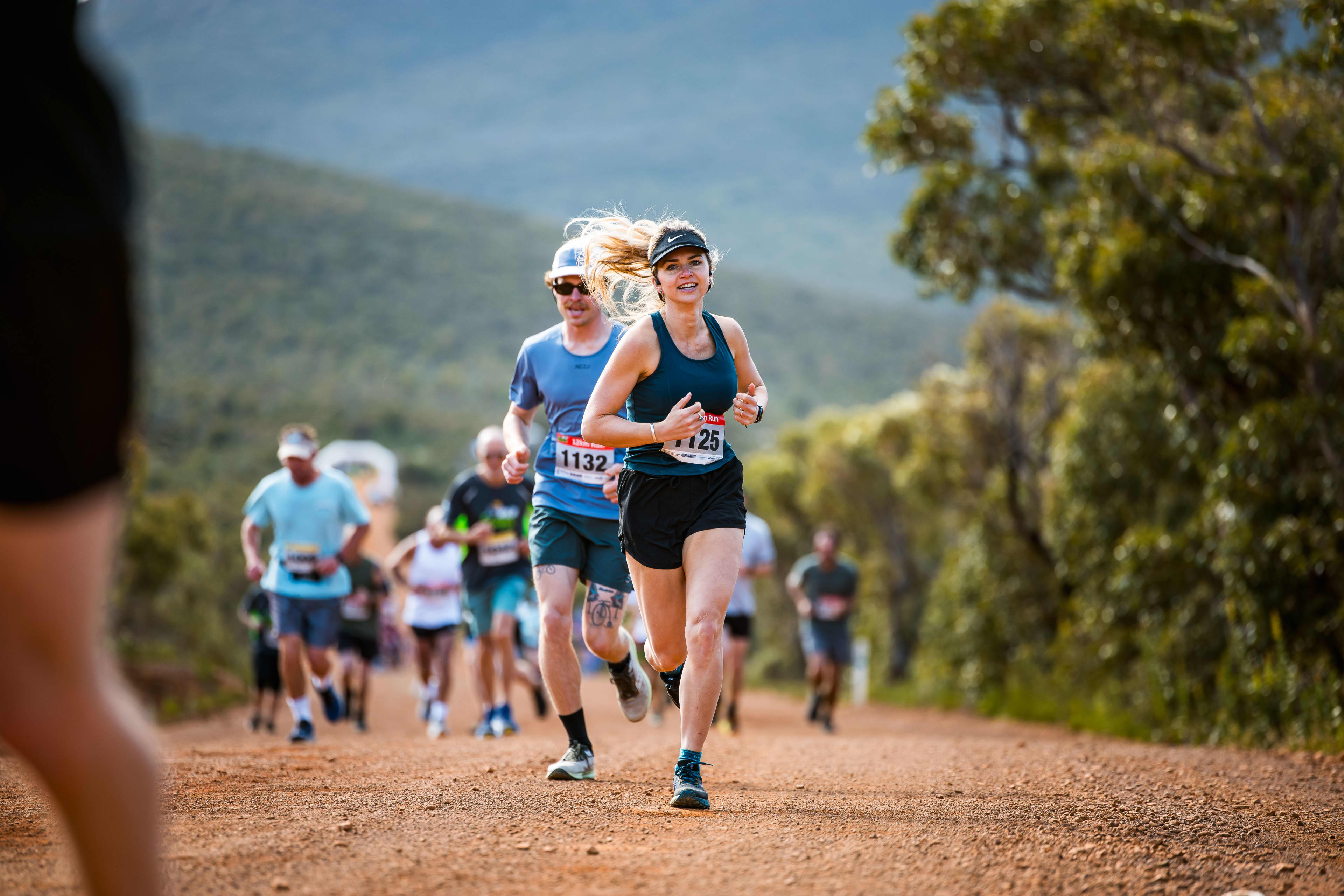 Crowd of people running on trail with bushland and mountain scenery