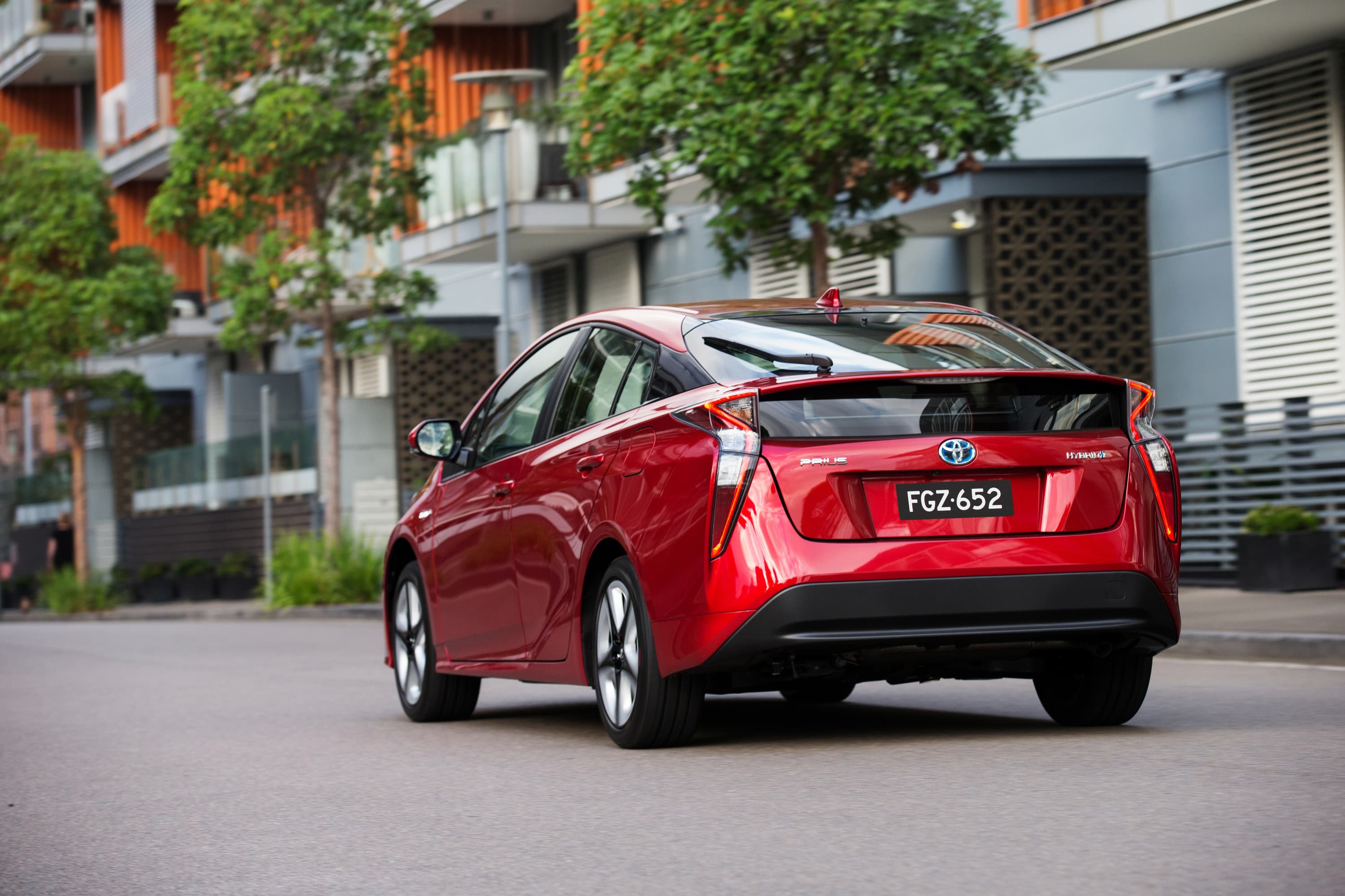 A red Toyota Prius parked outside modern townhouses.