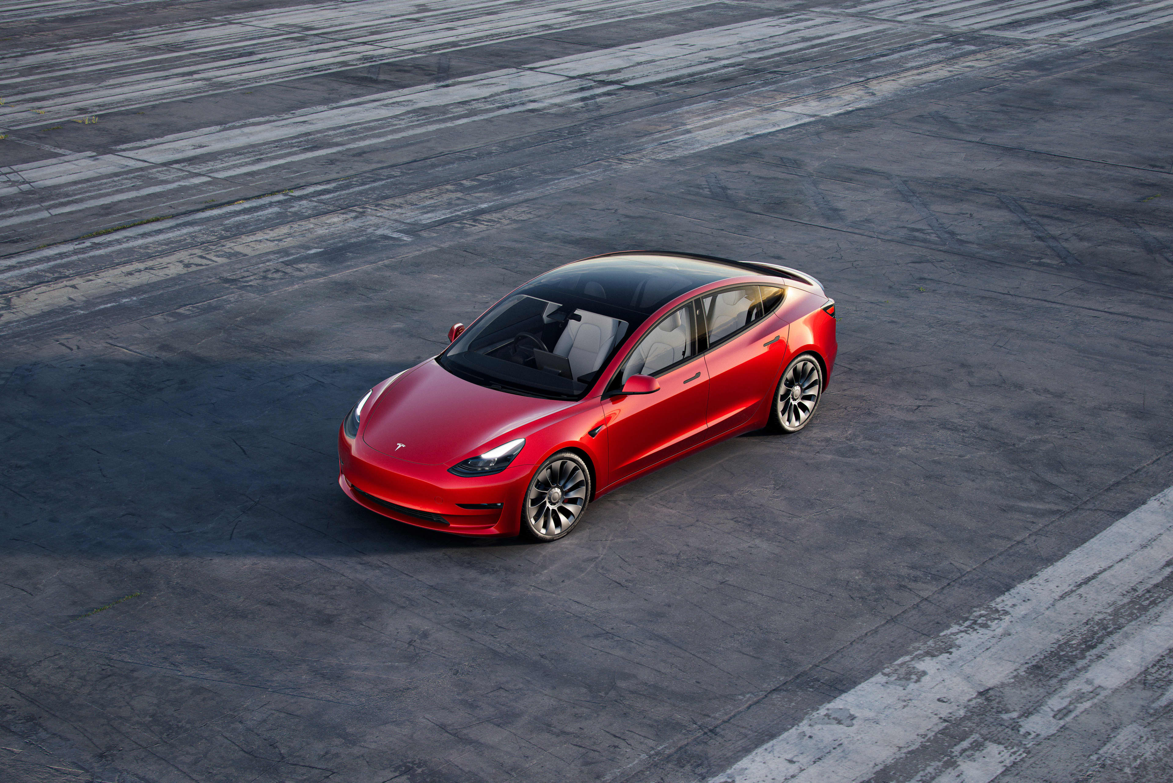 A red Tesla Model 3 parked on a dark tarmac.