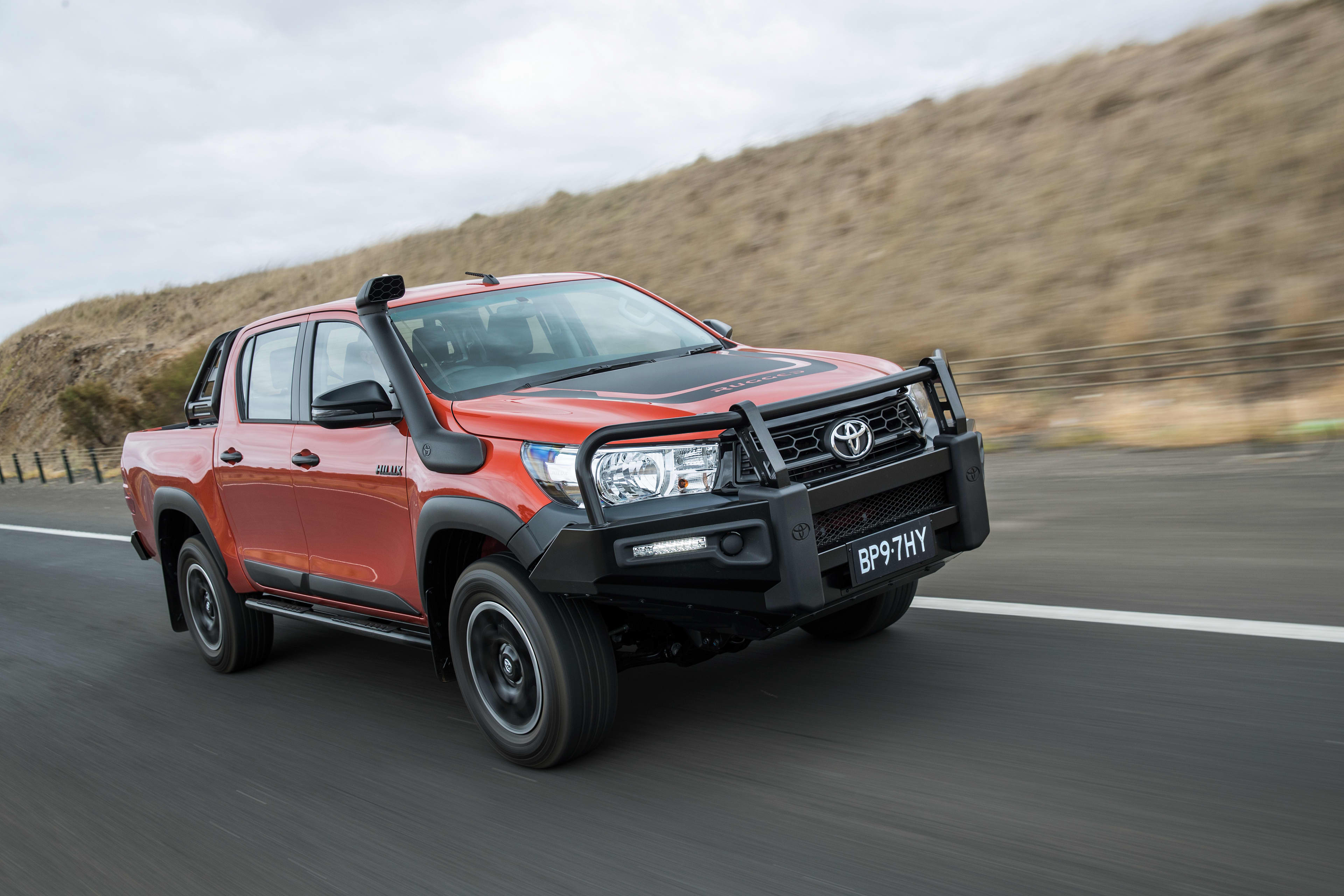 A red Toyota HiLux driving on a country road.