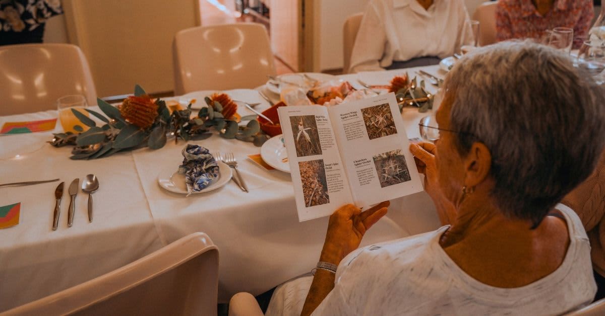 Woman reading wildflower book while at long table lunch