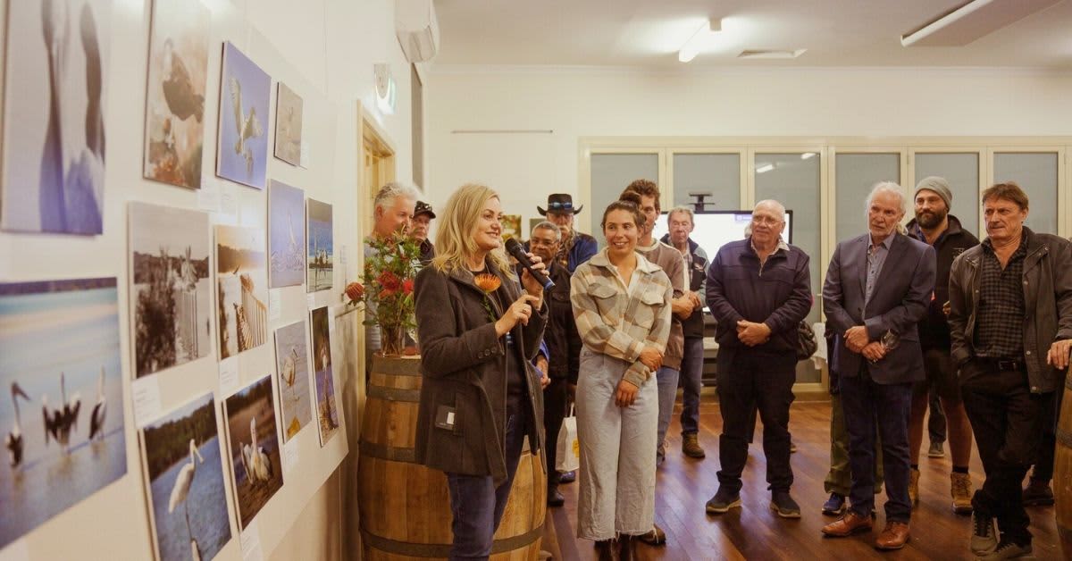 A group of people gather around a woman speaking in an art gallery