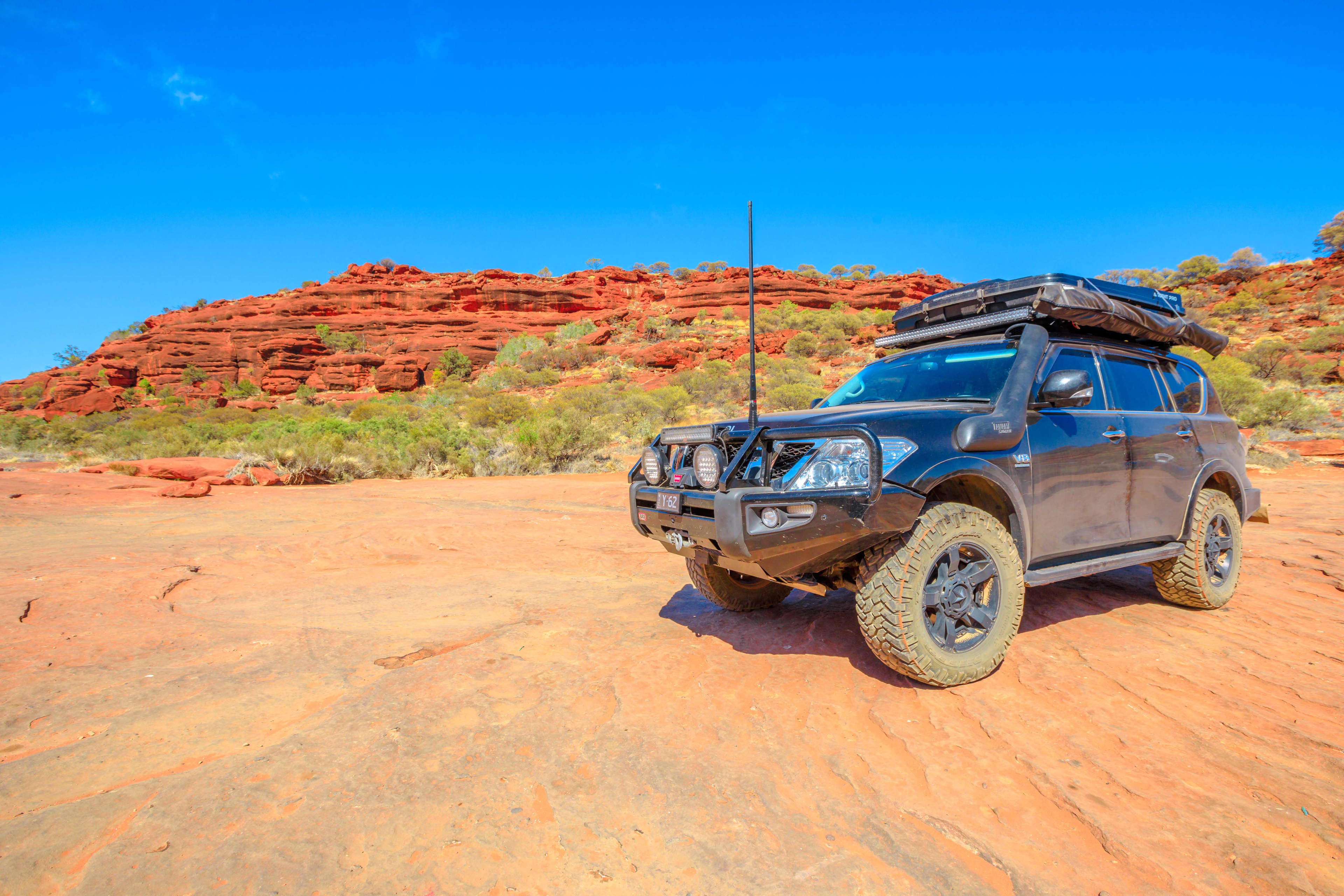 A black 4WD with a rooftop platform parked in red dirt clearing