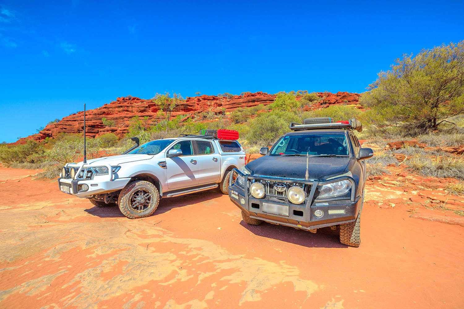 Two 4WD vehicles parked side by side on red dirt clearing