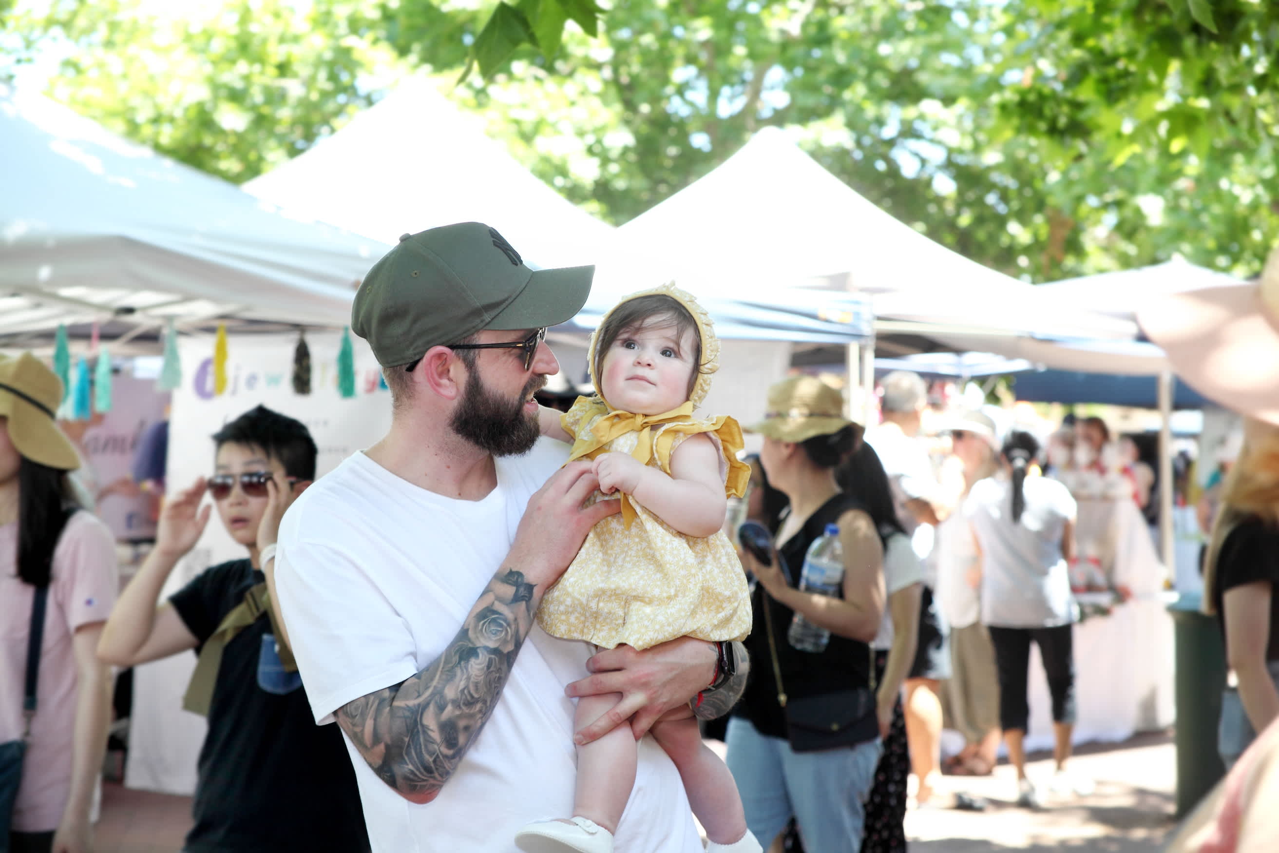 Father and young child looking at trees with market stalls in background