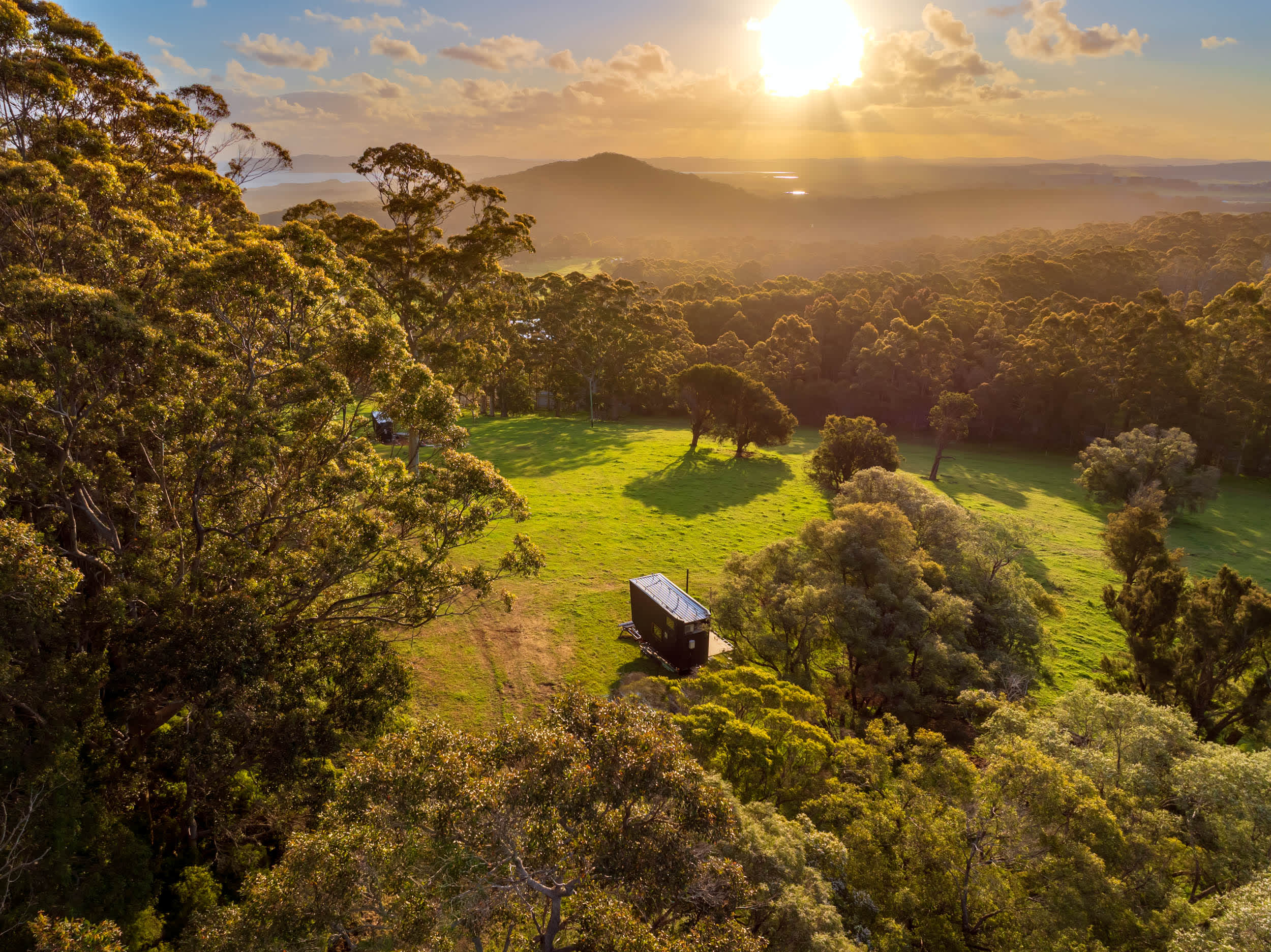 An aerial view of a tiny cabin in a lush green landscape