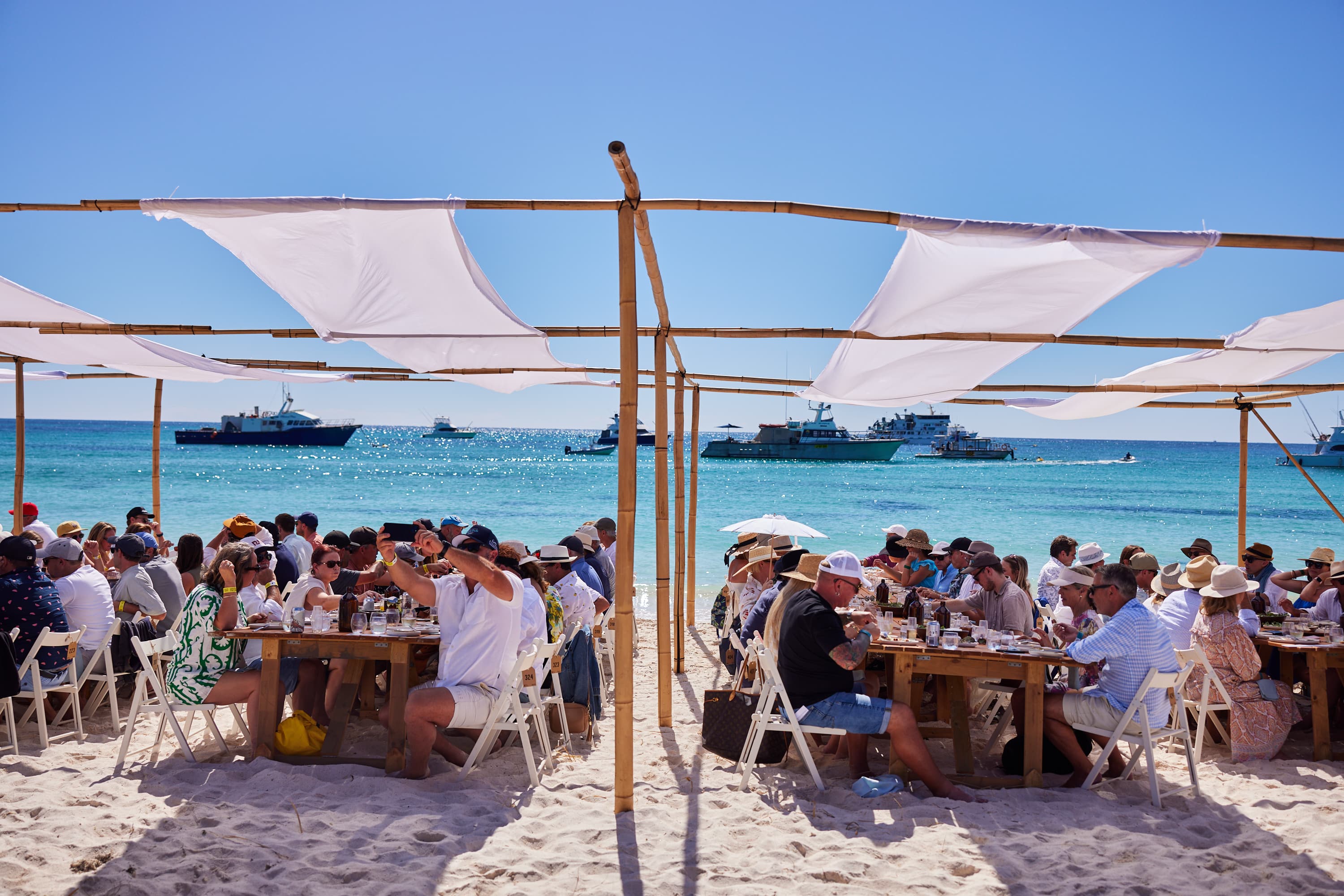 People dining on tables on the beach.
