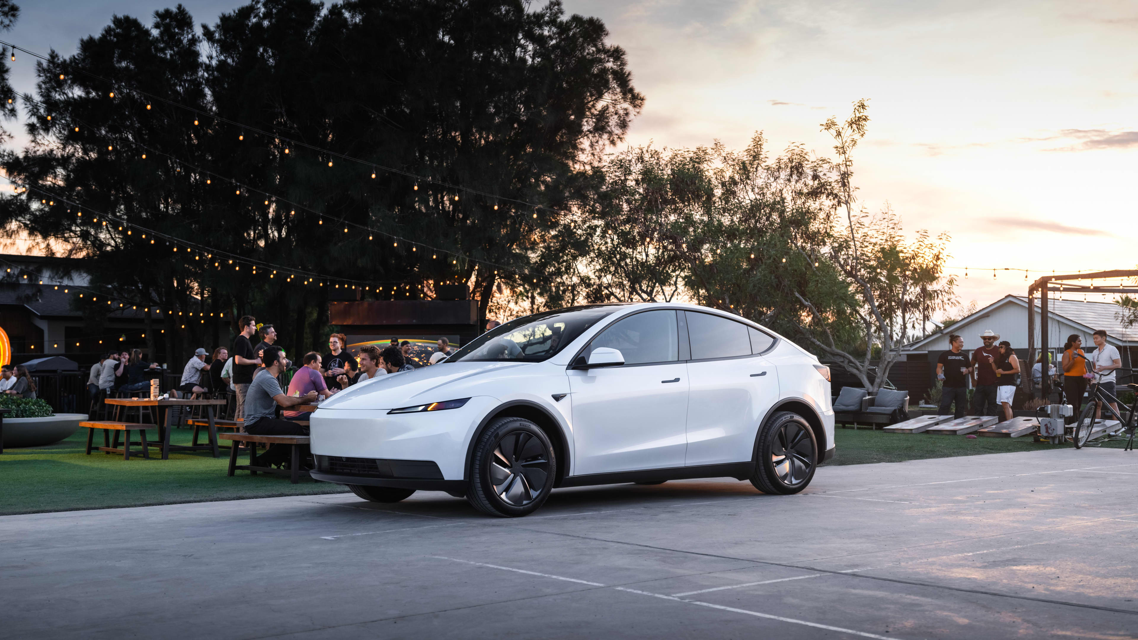 A white Tesla Model Y parked close to people eating at outdoor tables