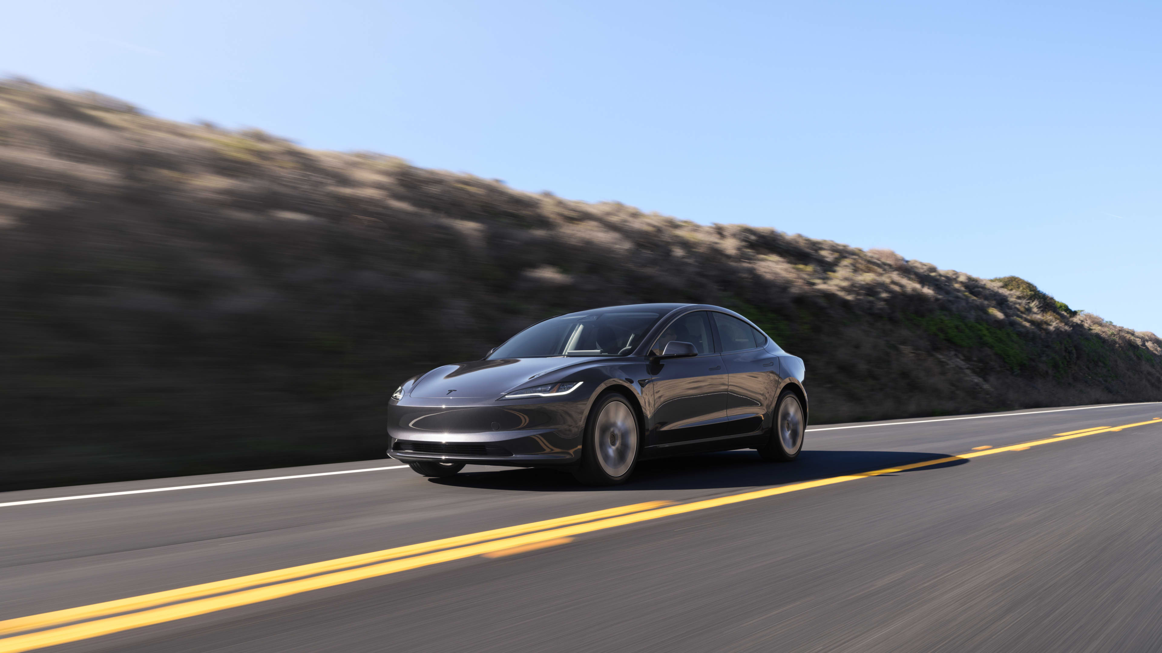 A dark grey Tesla Model 3 driving on a country road