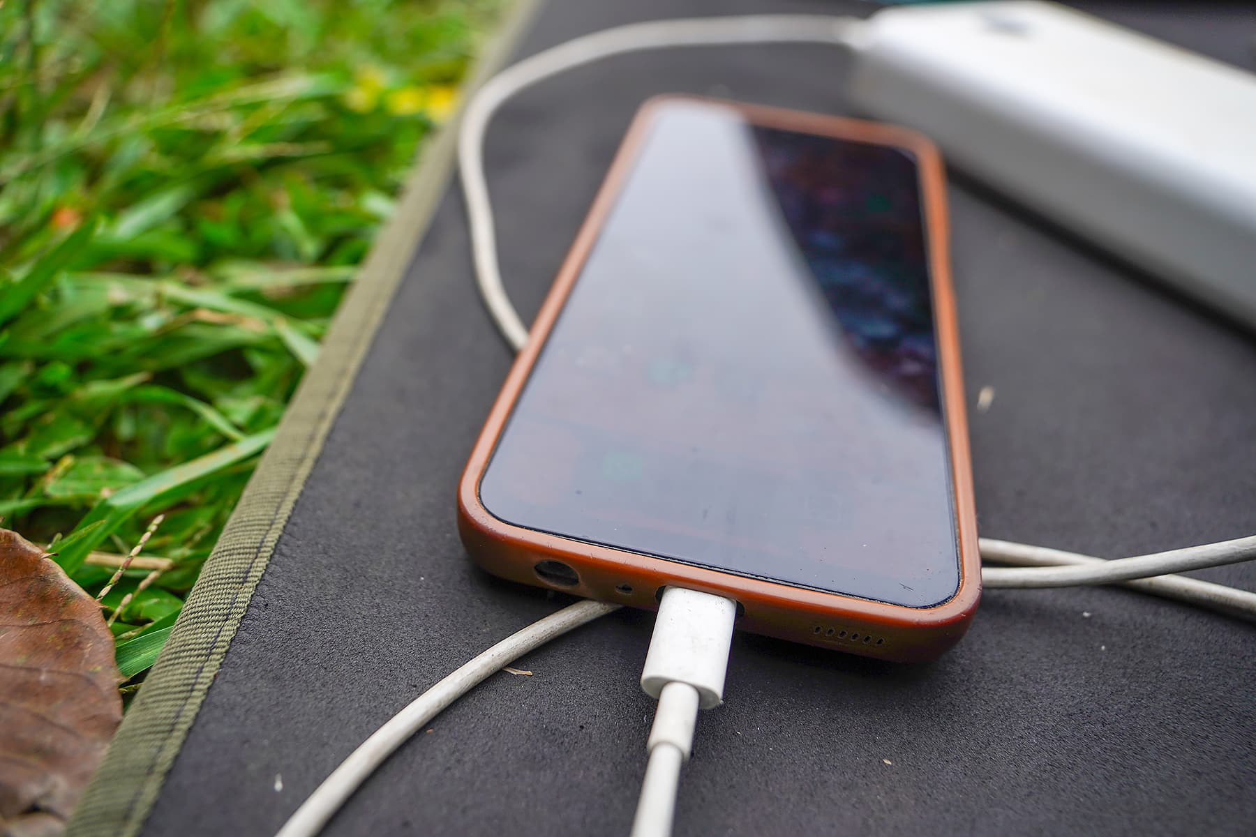 A mobile phone charging on the ground outdoors