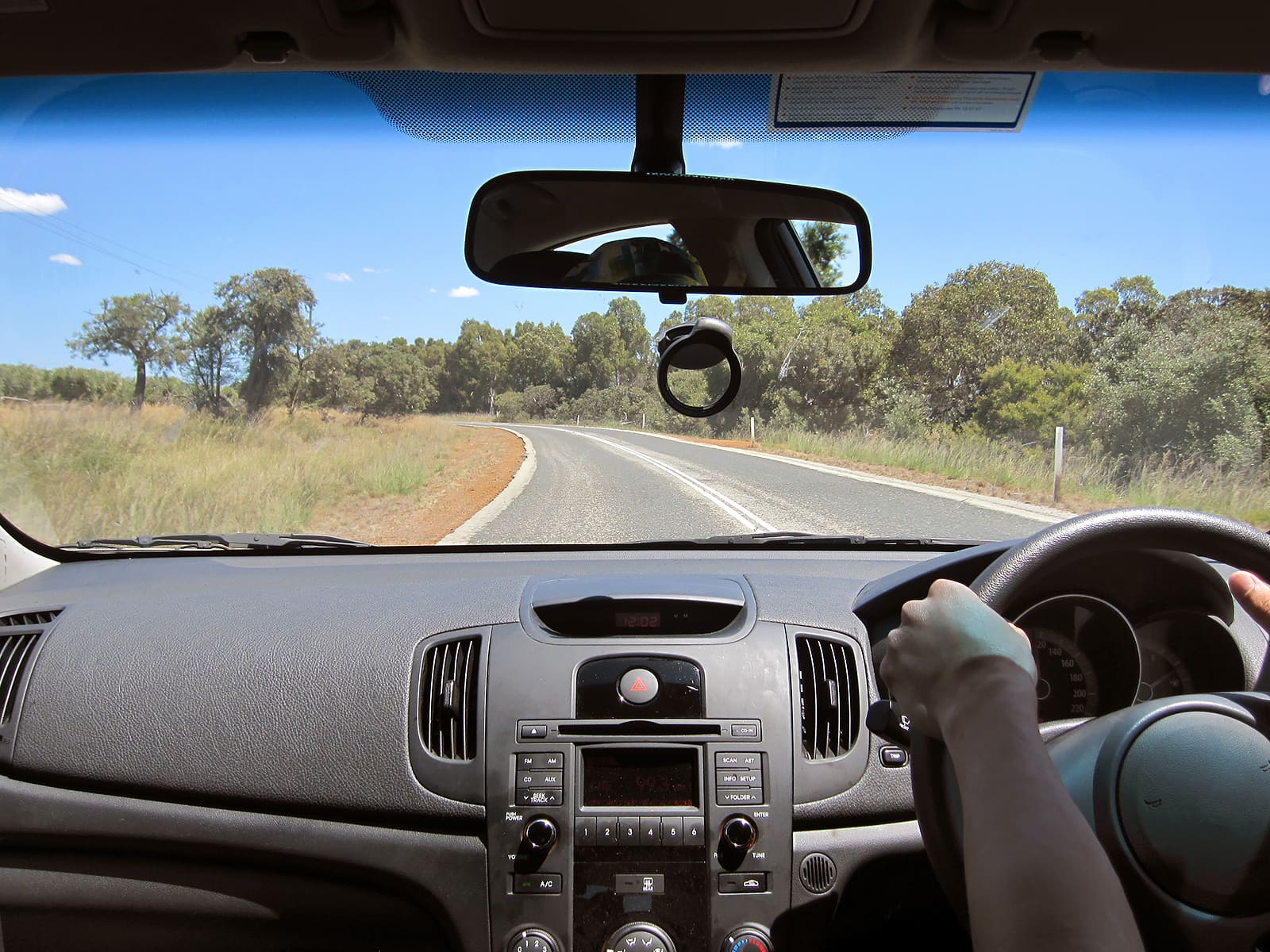 Seen from inside a car cabin a woman's hands are on the steering wheel driving on a country road