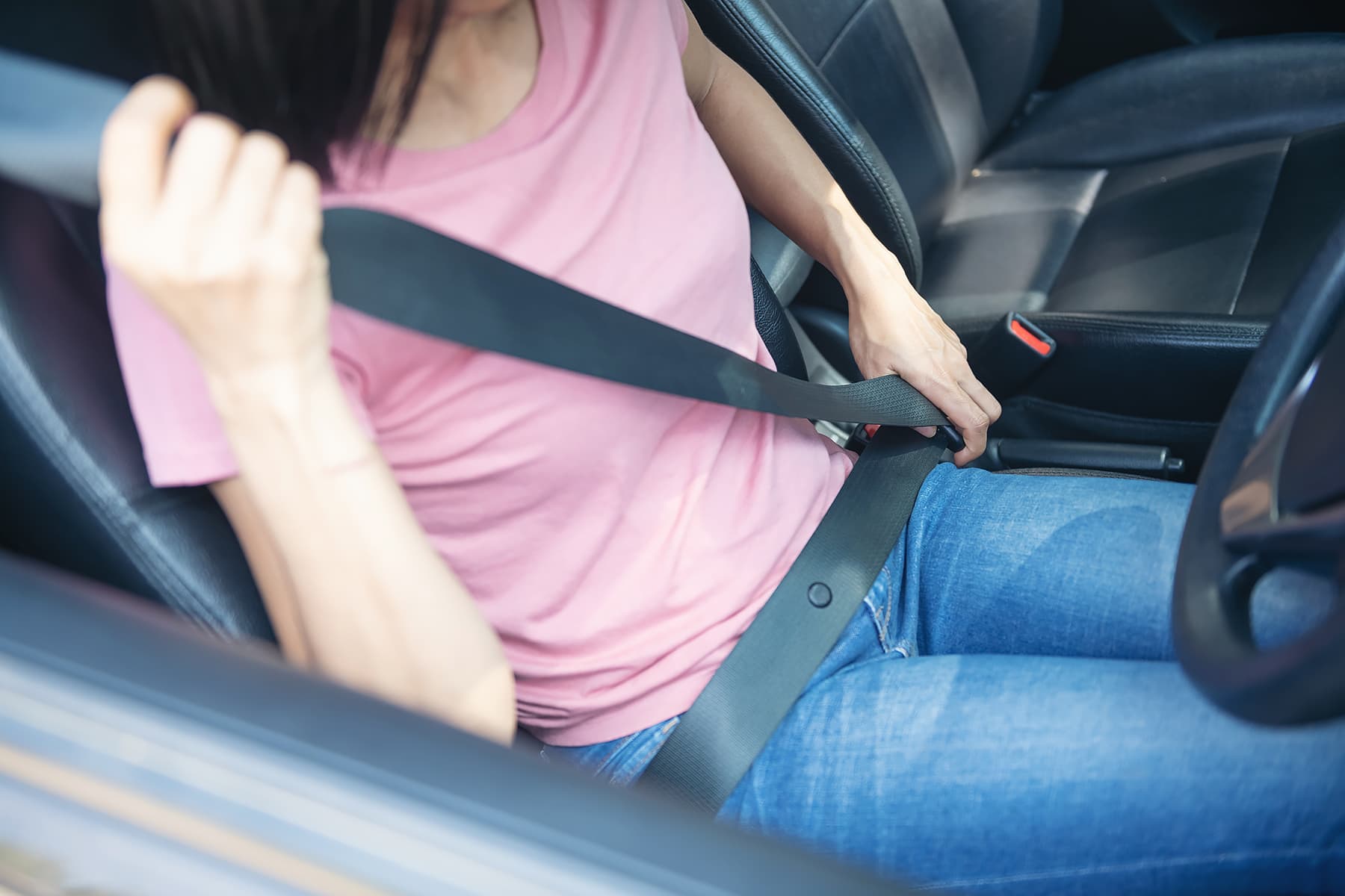 A woman putting on a seatbelt in the driver's seat of a car