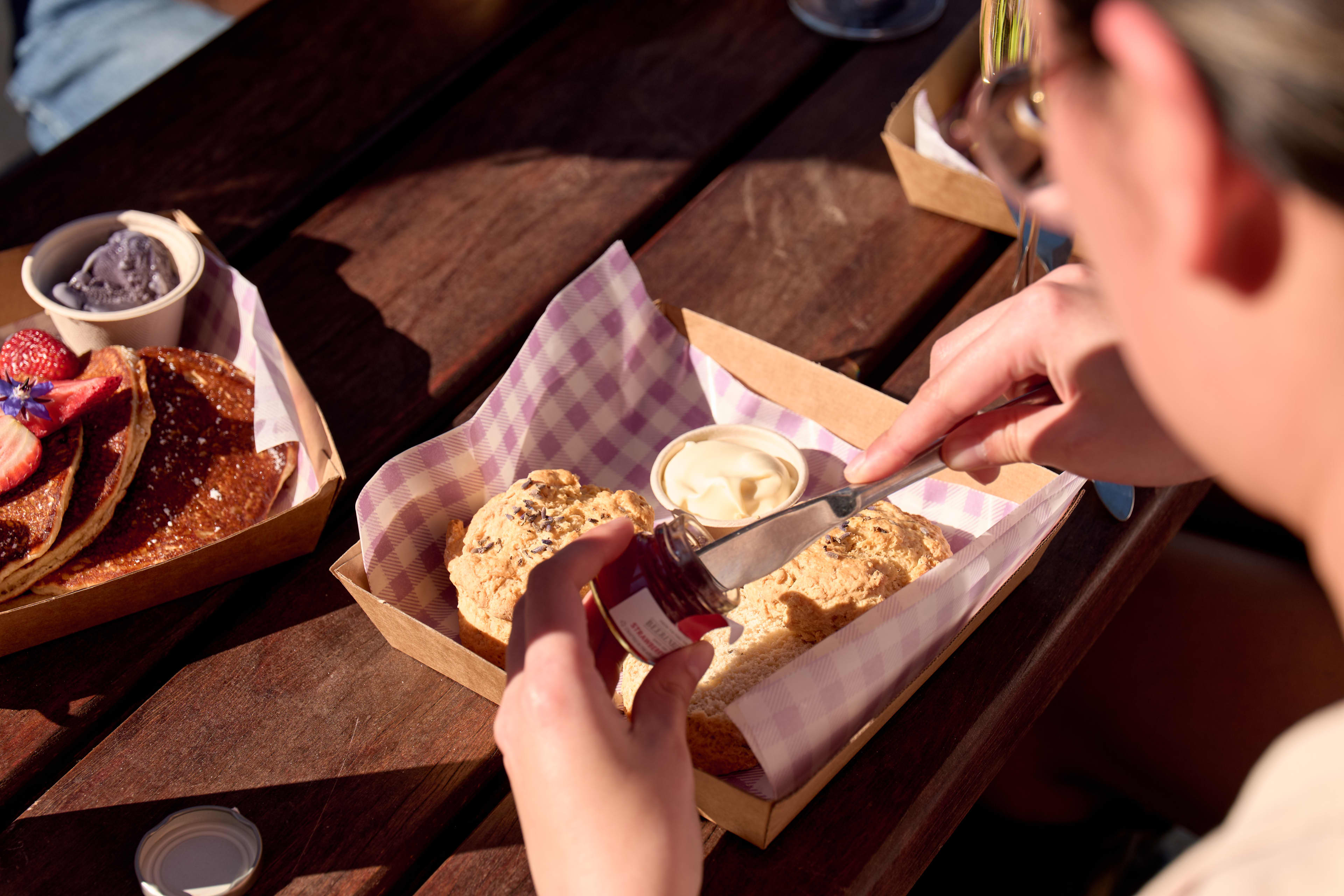 Person with knife getting jam out of jar to spread on scones