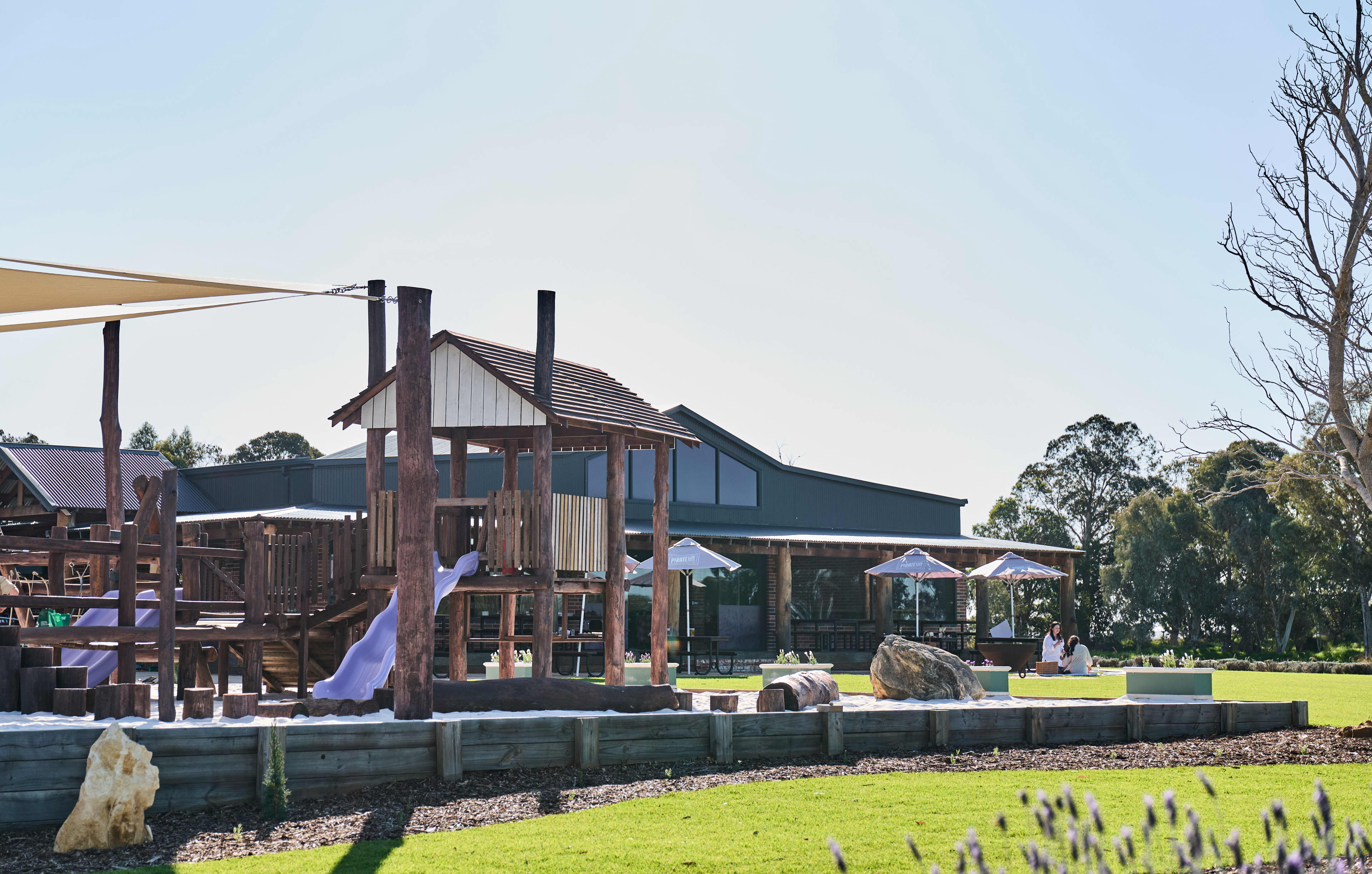Outdoor playground with dining venue in background with umbrellas on a deck