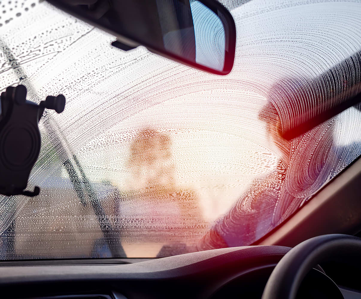 A person washing a windscreen seen from inside the car