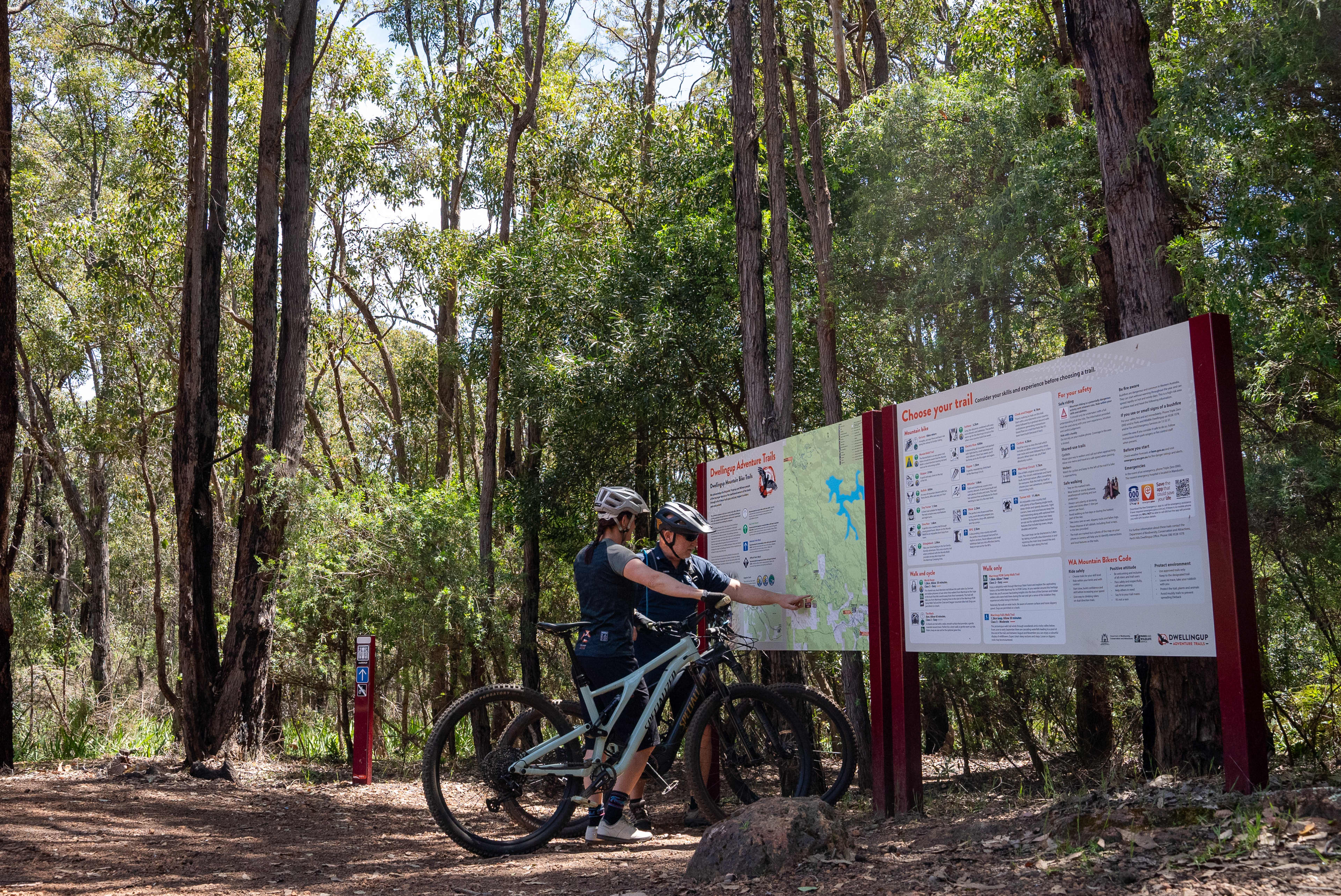 A person on a mountain bike in the forest in front of a large mountain bike trails sign