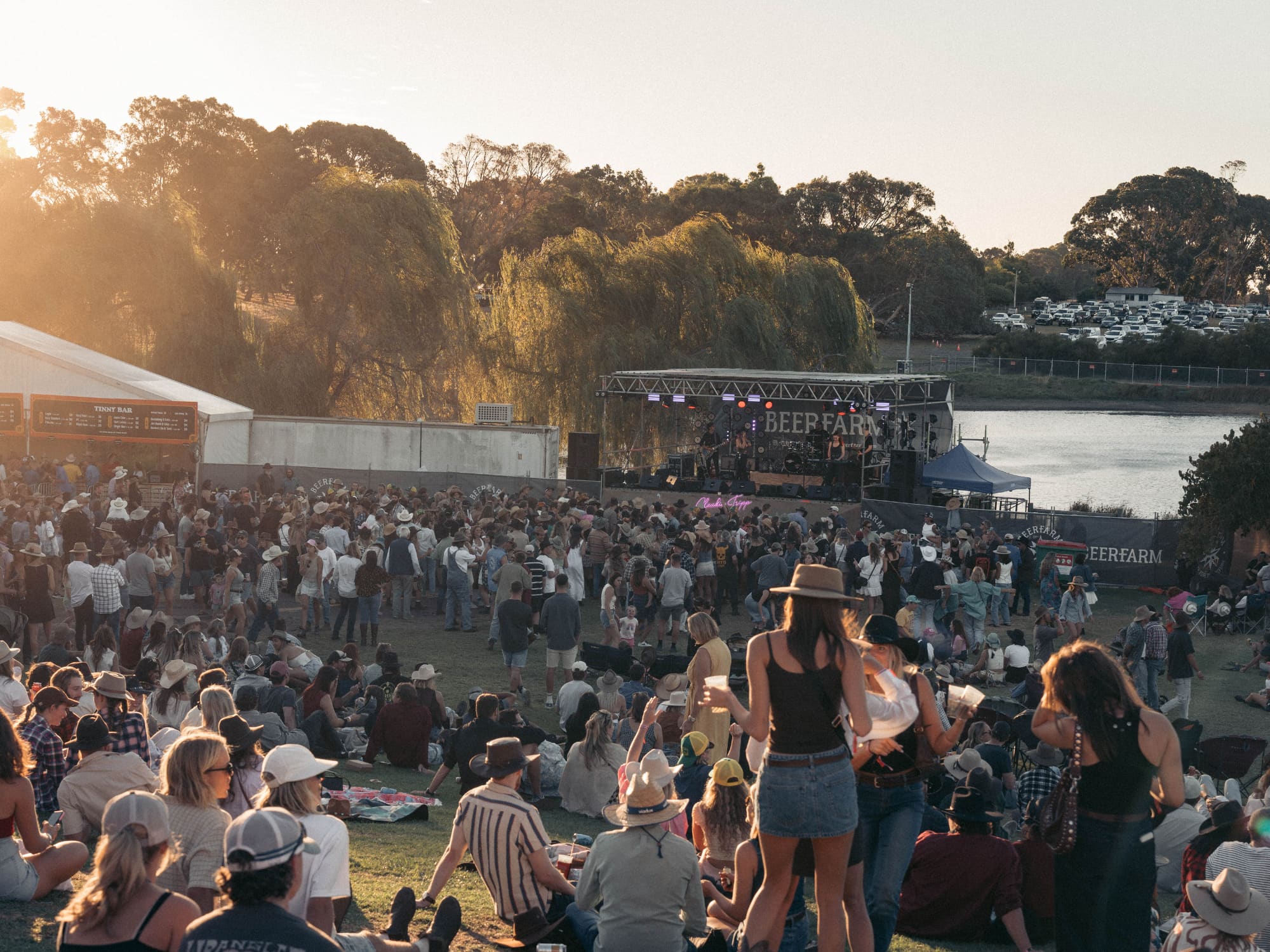 Festival of people at sundown event outside with marquees and grass lawns