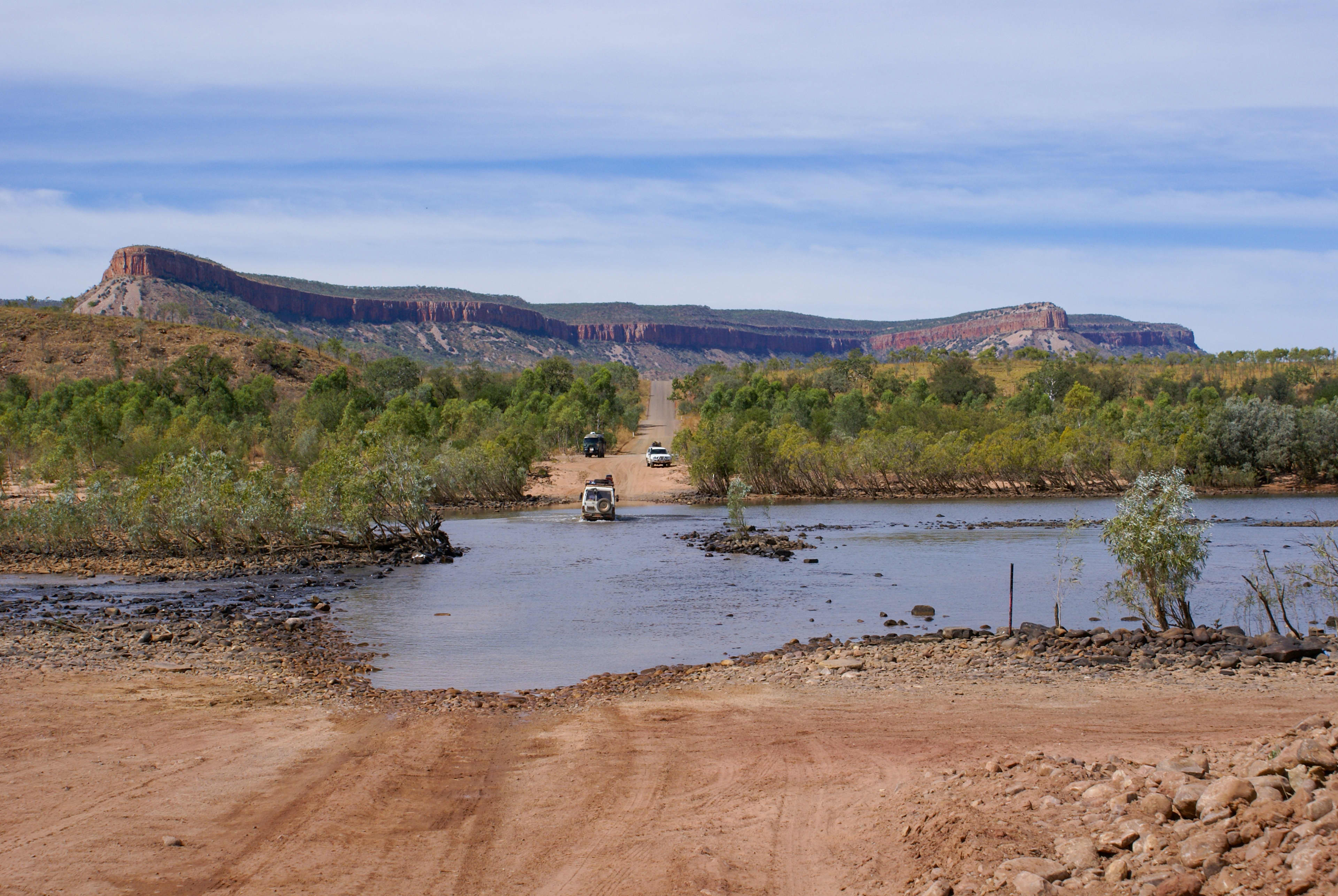 Two four-wheel drive vehicles crossing a river in the WA outbak.