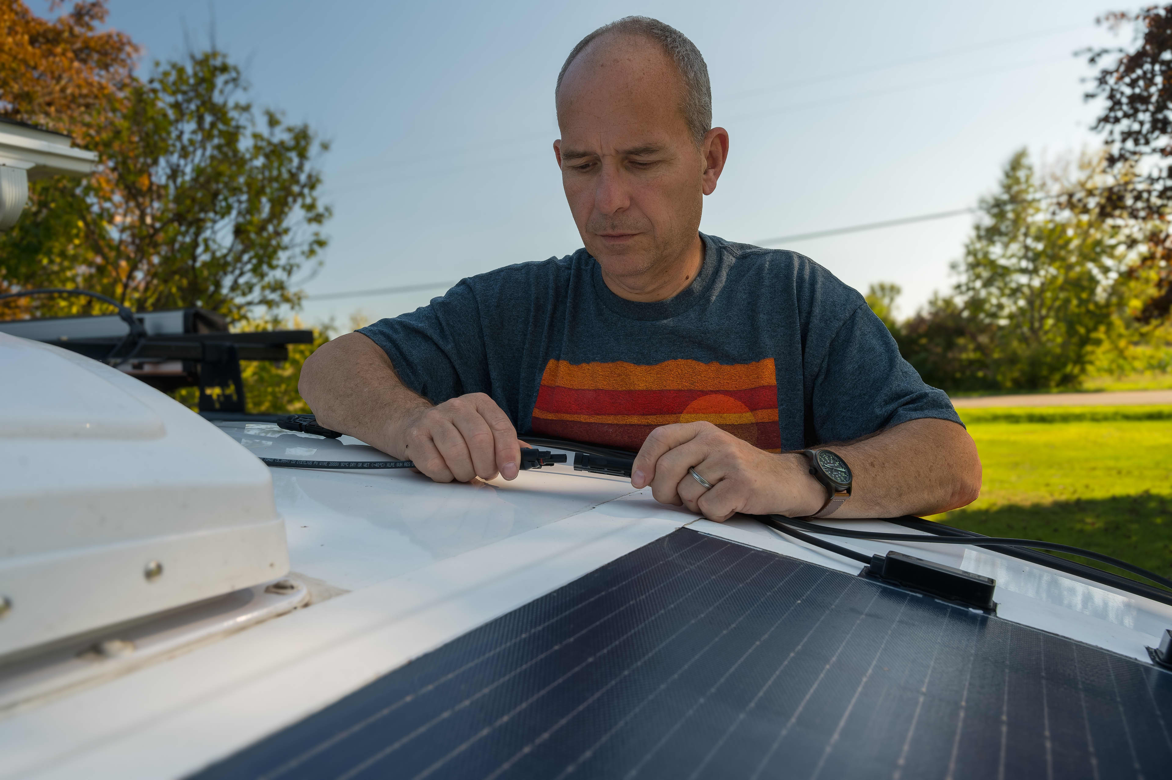 A person is connecting some wiring from solar panels on a caravan roof.