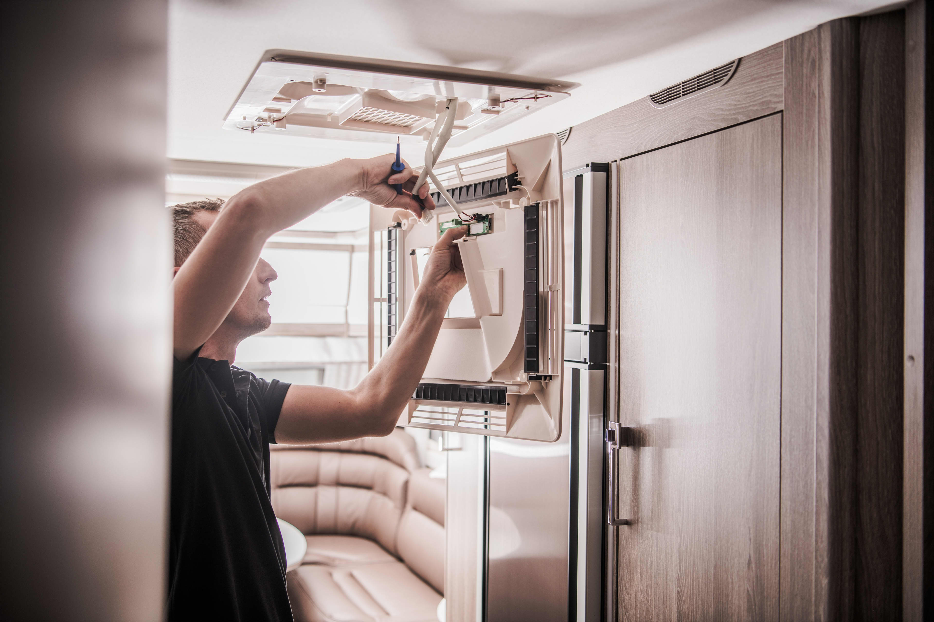 A person is working on an electrical appliance on the wall of a caravan