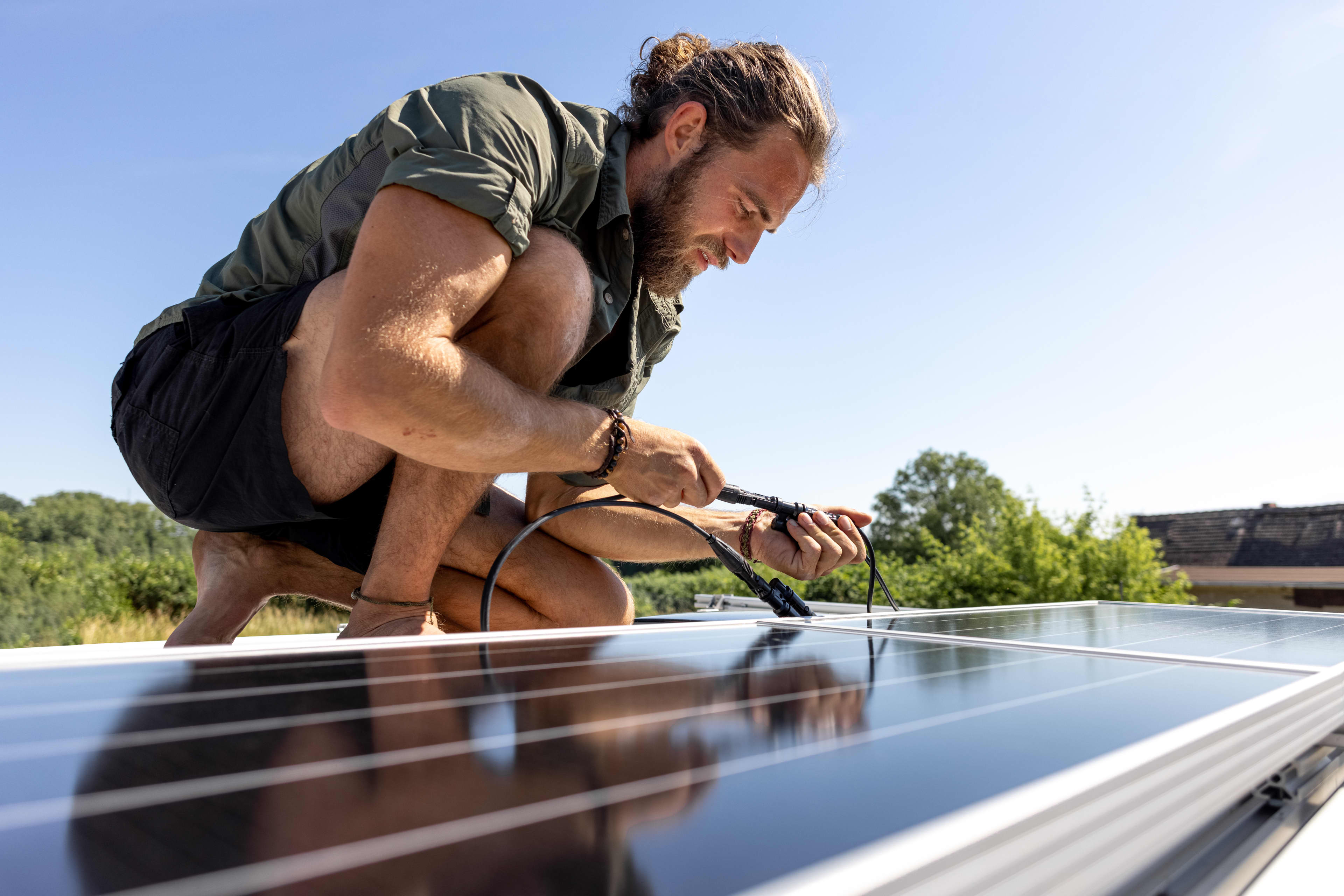 A person is crouching on a caravan roof connecting some wiring.