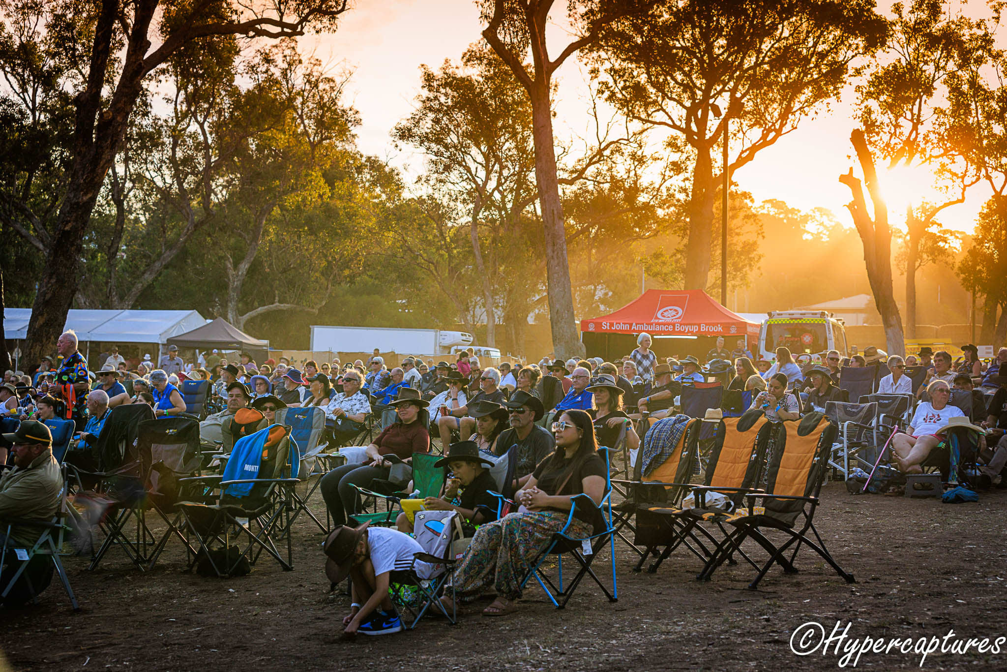 A crowd of people sitting on camp chairs, with the sun setting in the background.