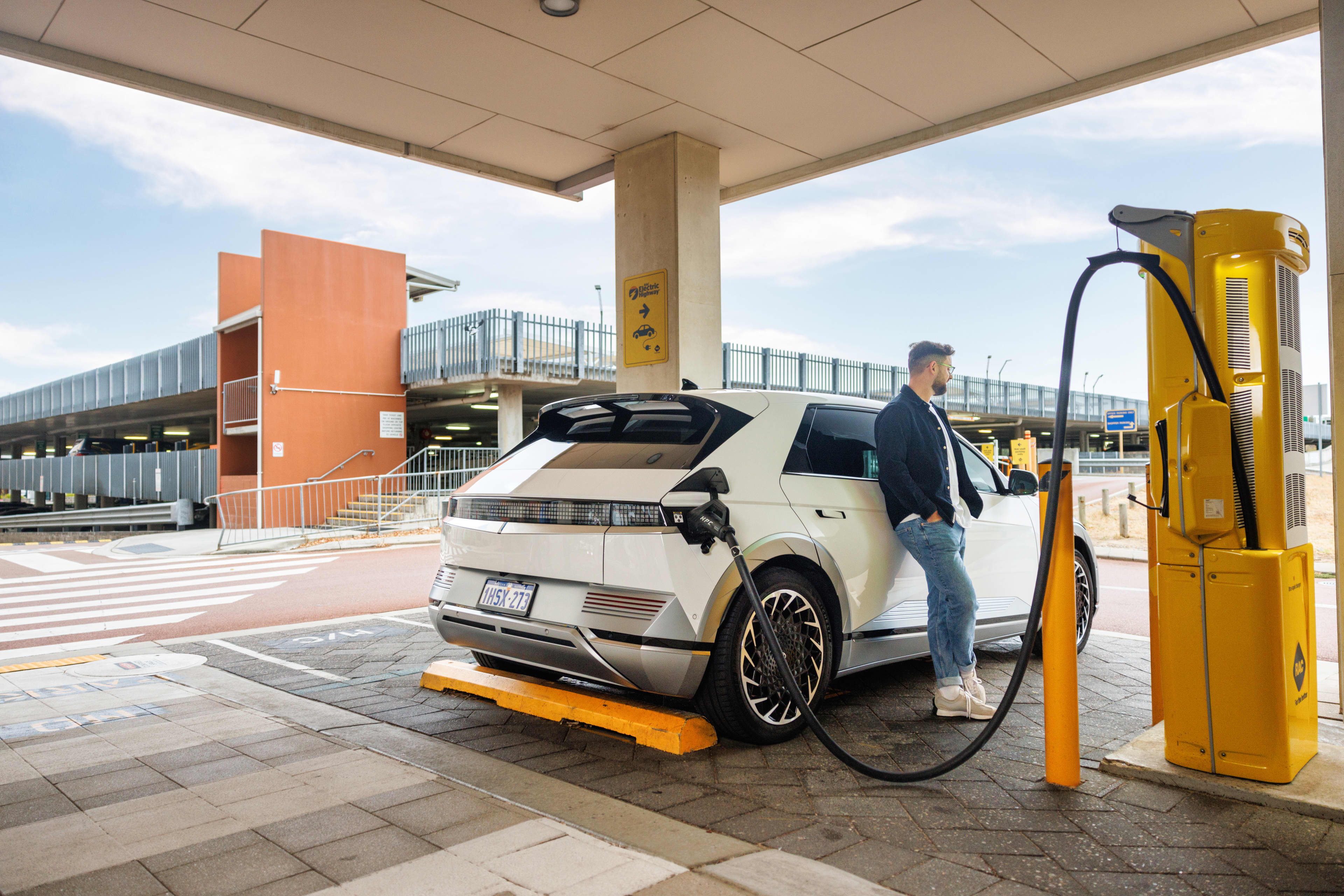 EV owner leaning against electric vehicle while it is charging