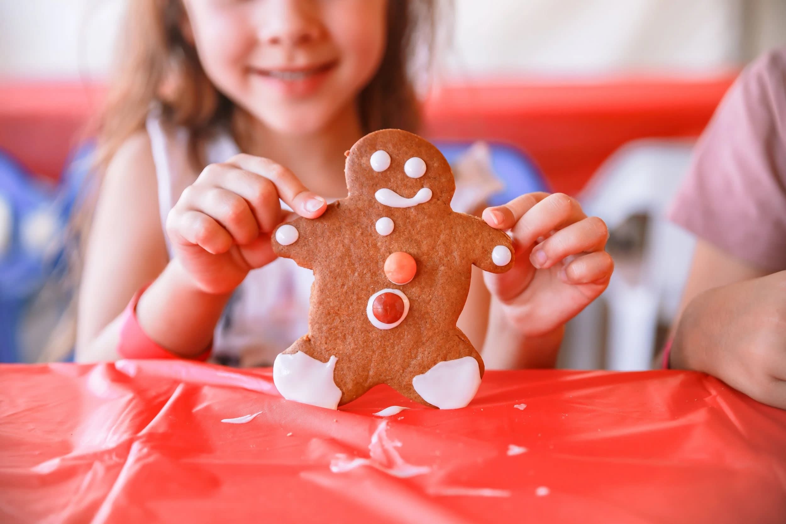 A happy young girl holding a decorated gingerbread man over a red mat.